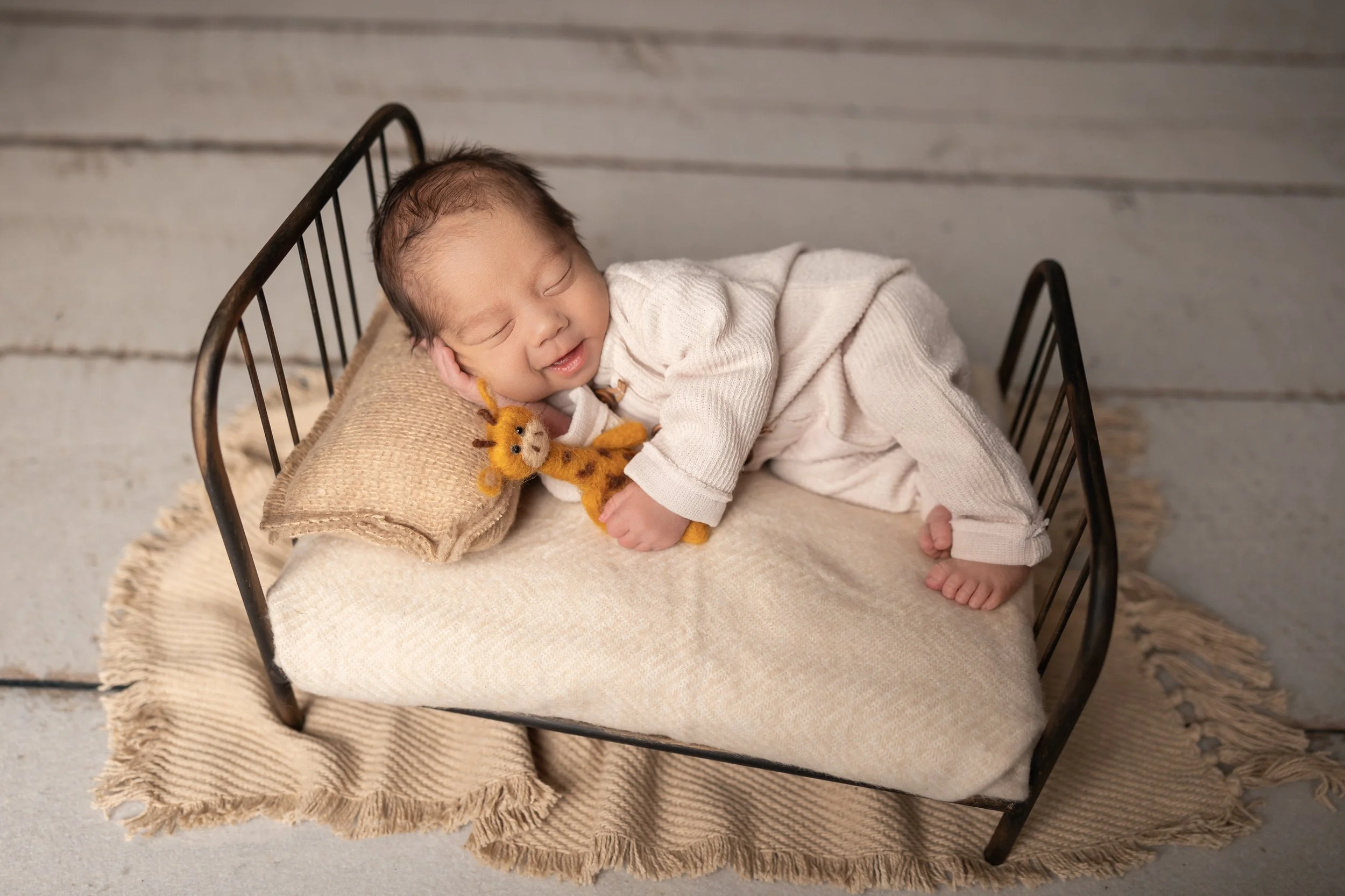 Sleeping newborn baby smiling while posed in a miniature bed prop during a studio newborn photography session in Austin, Texas.