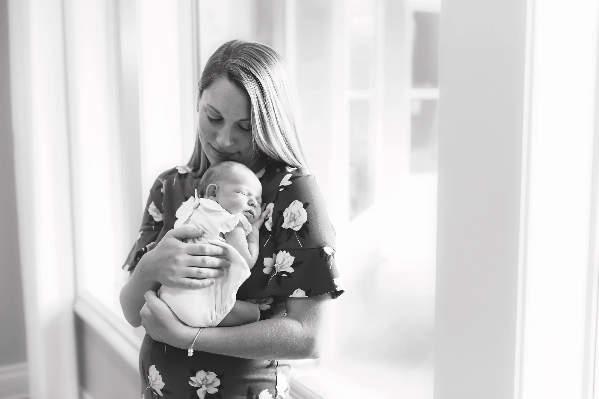 mom holding sleeping newborn in front of window