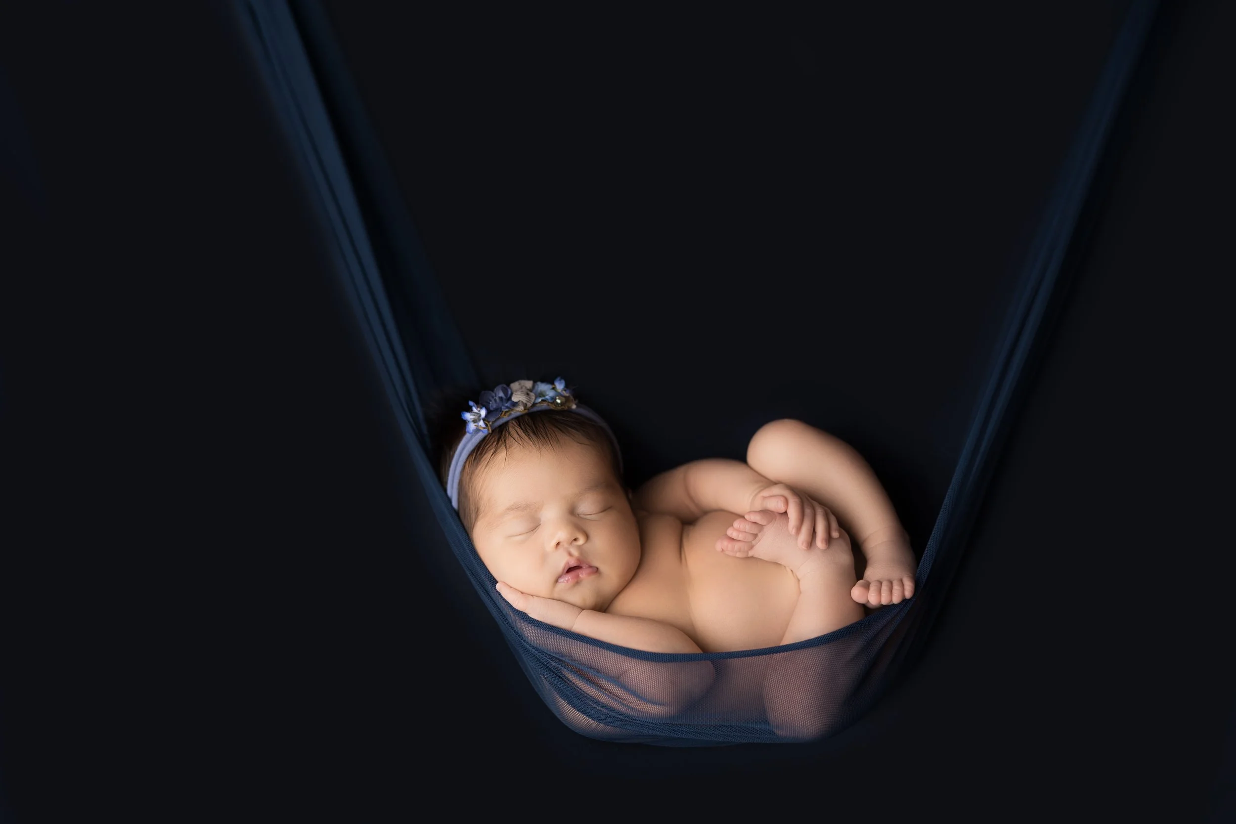 Sleeping newborn photographed in a fabric hammock using a safe composite technique by an experienced Austin newborn photographer.