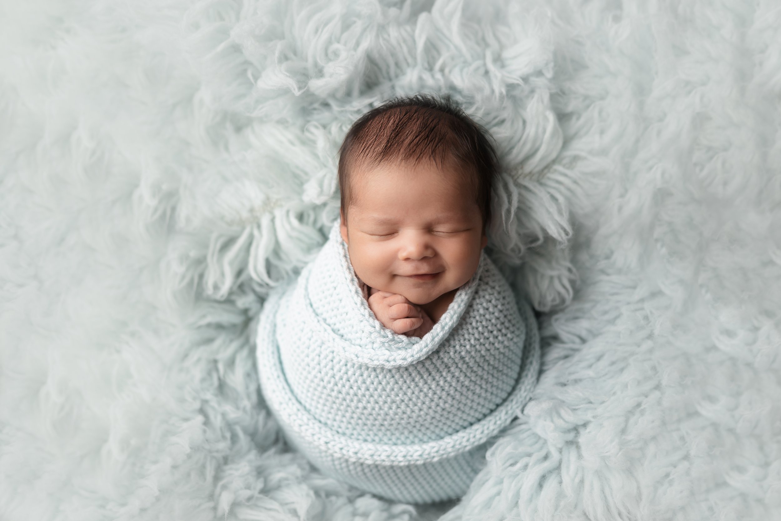 Newborn wrapped in a blue knit wrap demonstrating wrapping techniques taught during newborn photography mentoring.