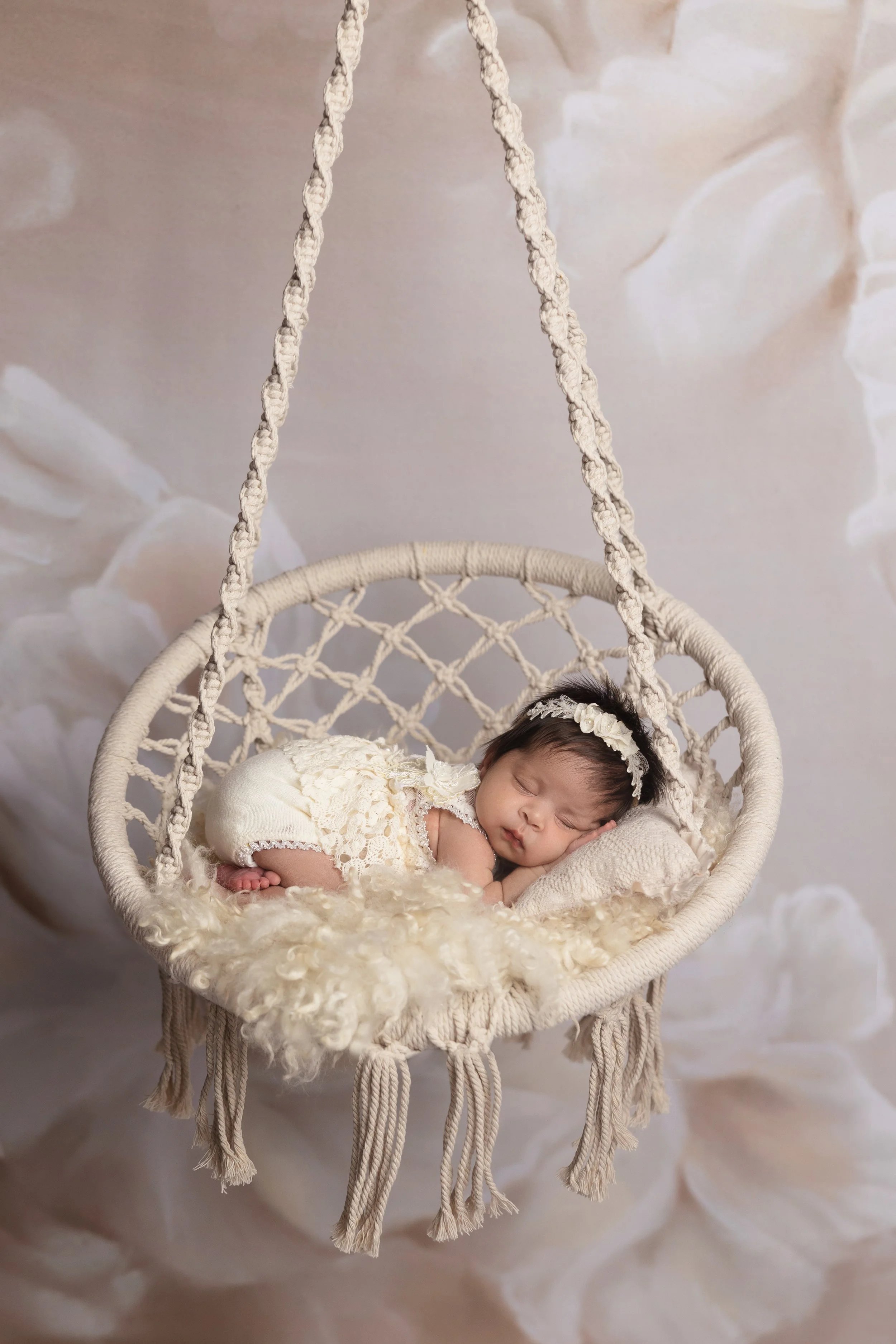 A sleeping newborn baby posed safely in a handcrafted hanging basket during a studio newborn session.