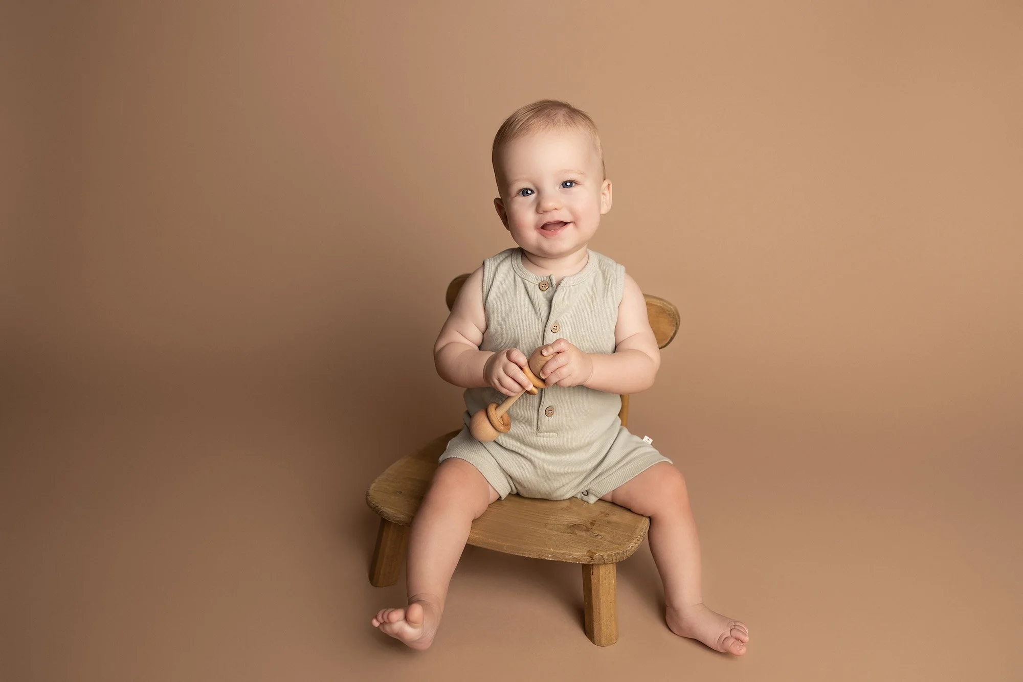 Baby sitting independently on a wooden chair during a neutral milestone photography session in Austin TX.