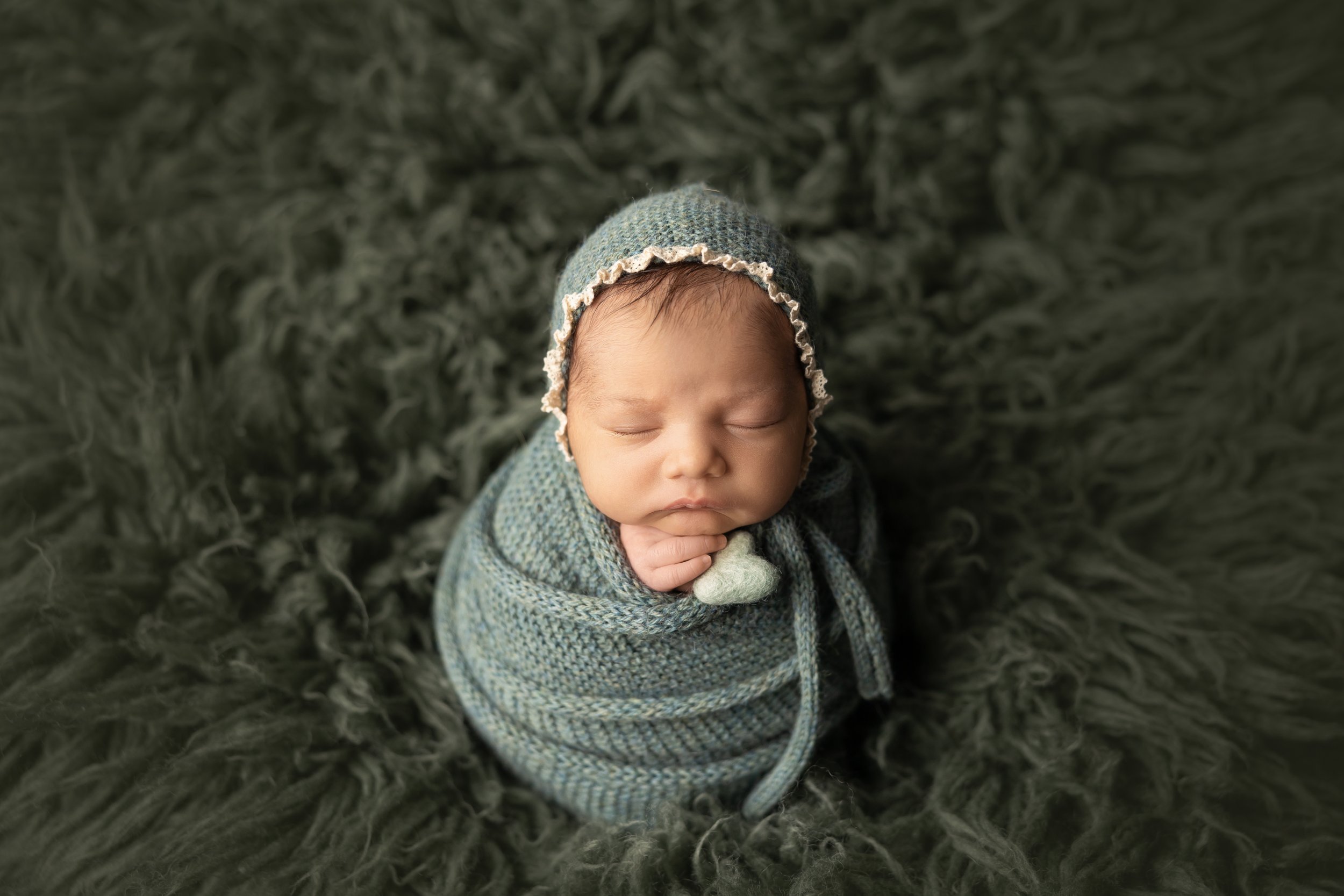 close up of newborn wrapped in green swaddle sleeping