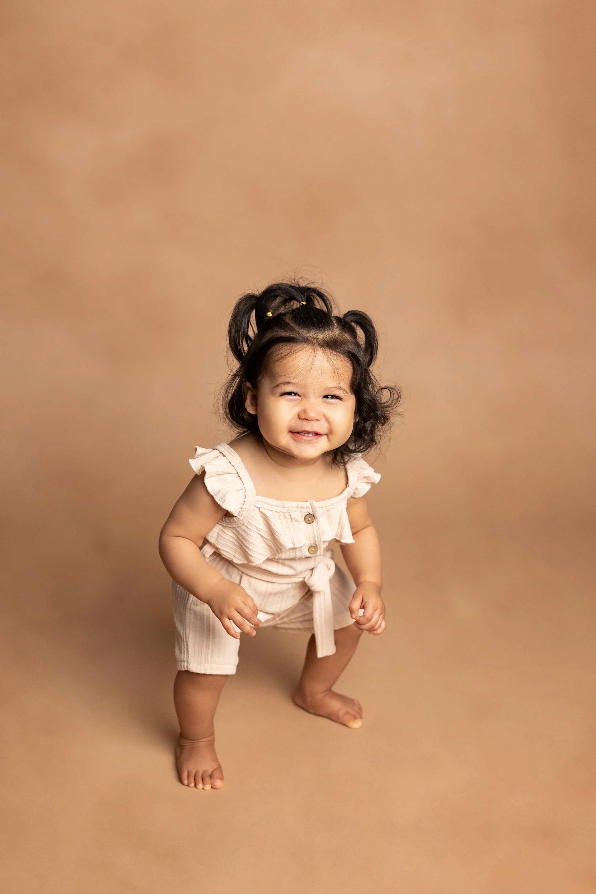 Smiling one-year-old girl standing during a milestone photography session in an Austin studio.