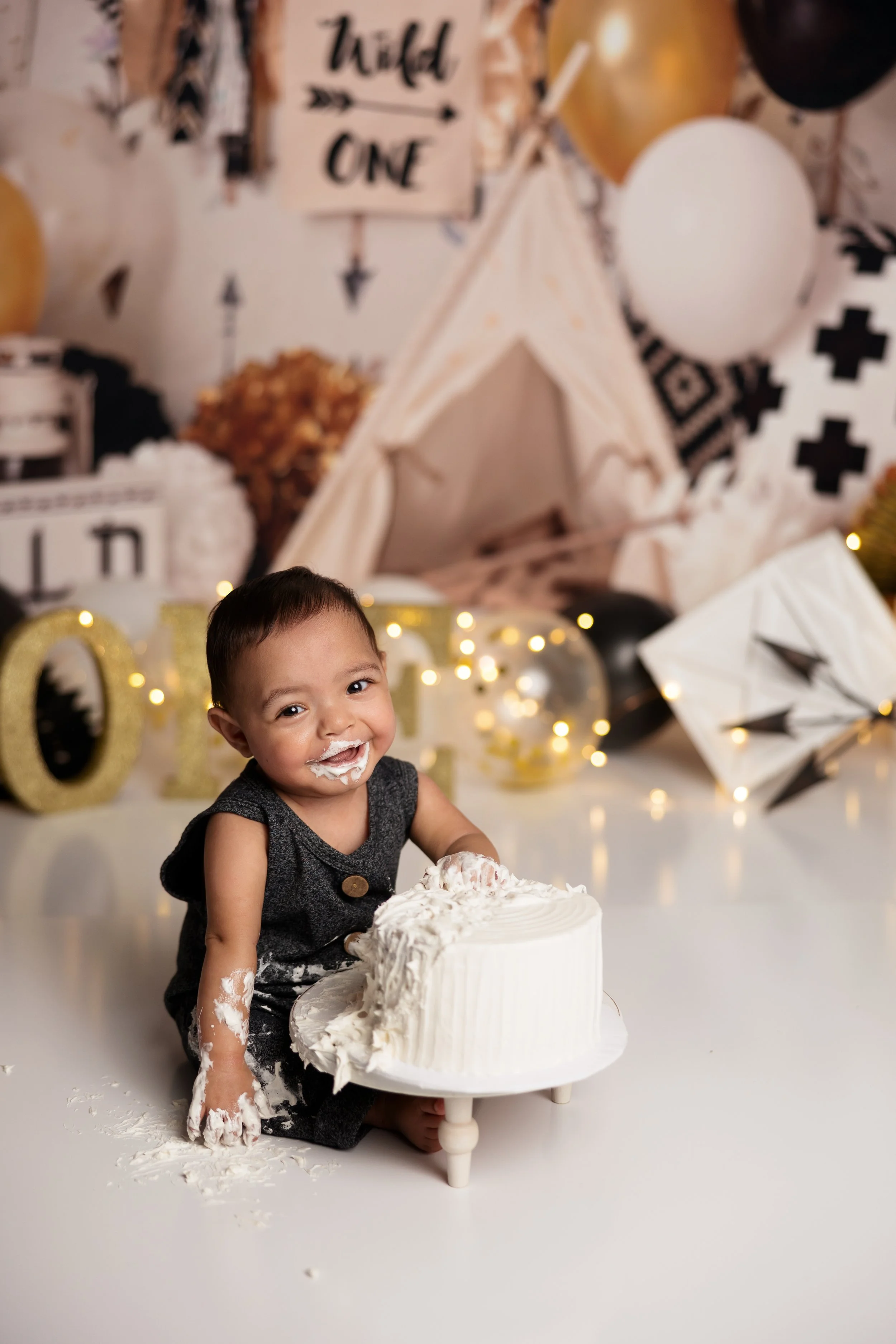 Smiling baby boy covered in frosting during a Wild One themed first birthday cake smash session.