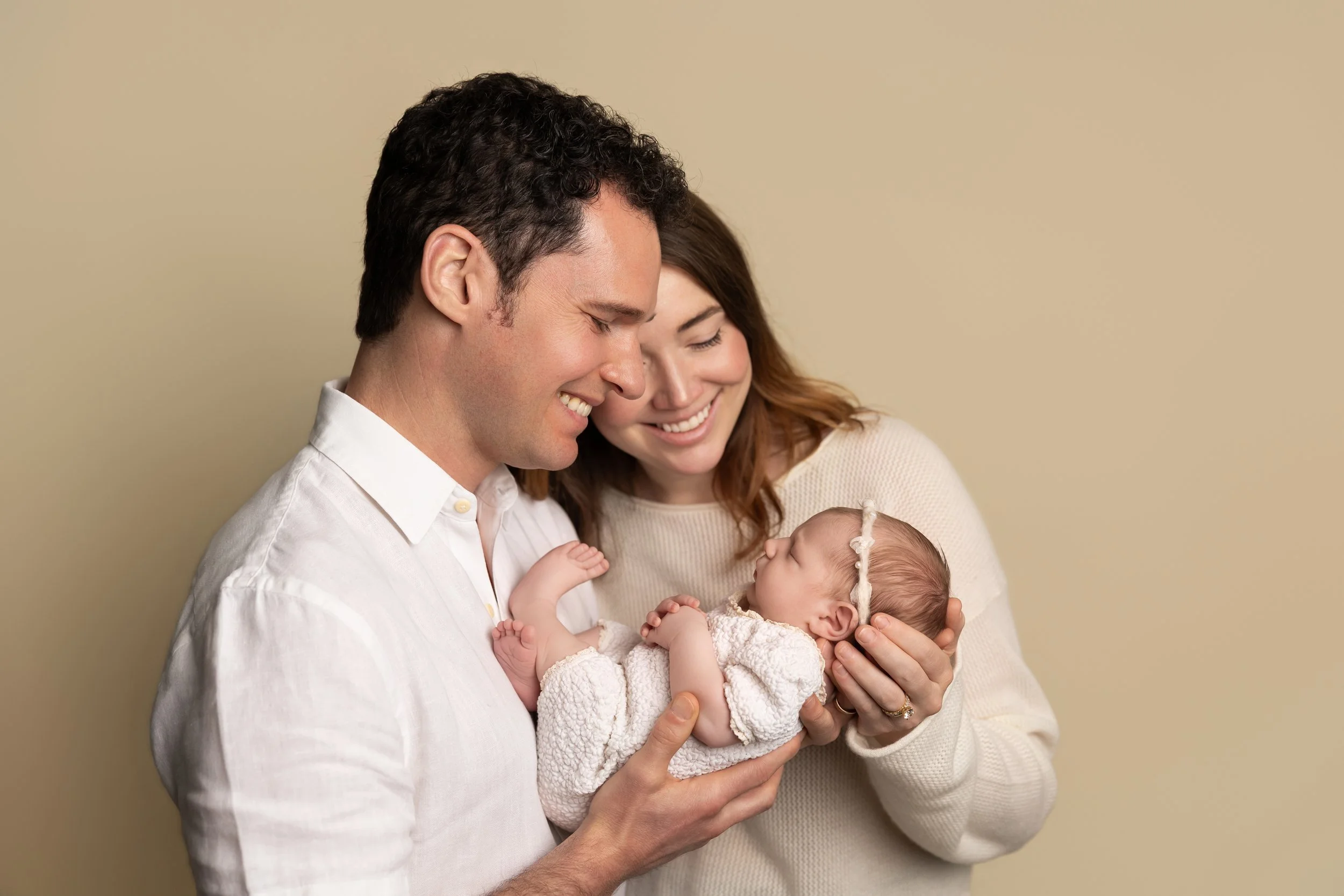 Parents wearing coordinated neutral clothing while holding their newborn during a studio newborn photography session.