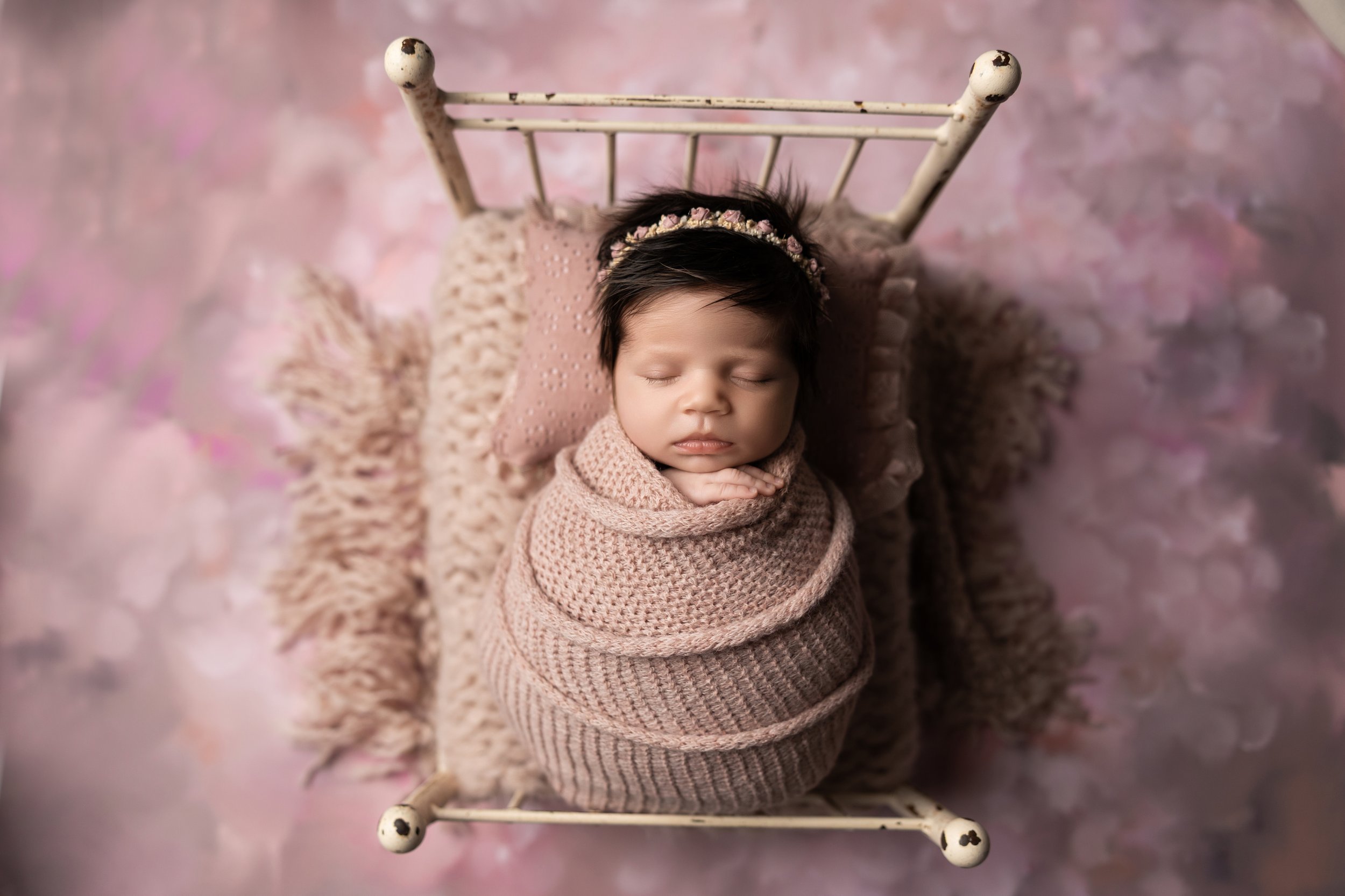 Fully wrapped newborn posed in a vintage newborn bed prop with coordinating backdrop, demonstrating one of the most versatile newborn photography props.