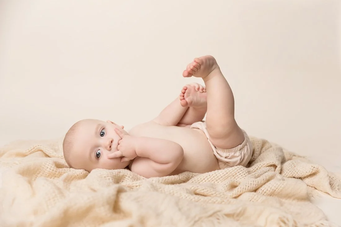 four month old boy lying on neutral blanket with fingers in mouth in University of Texas Longhorns hook 'em