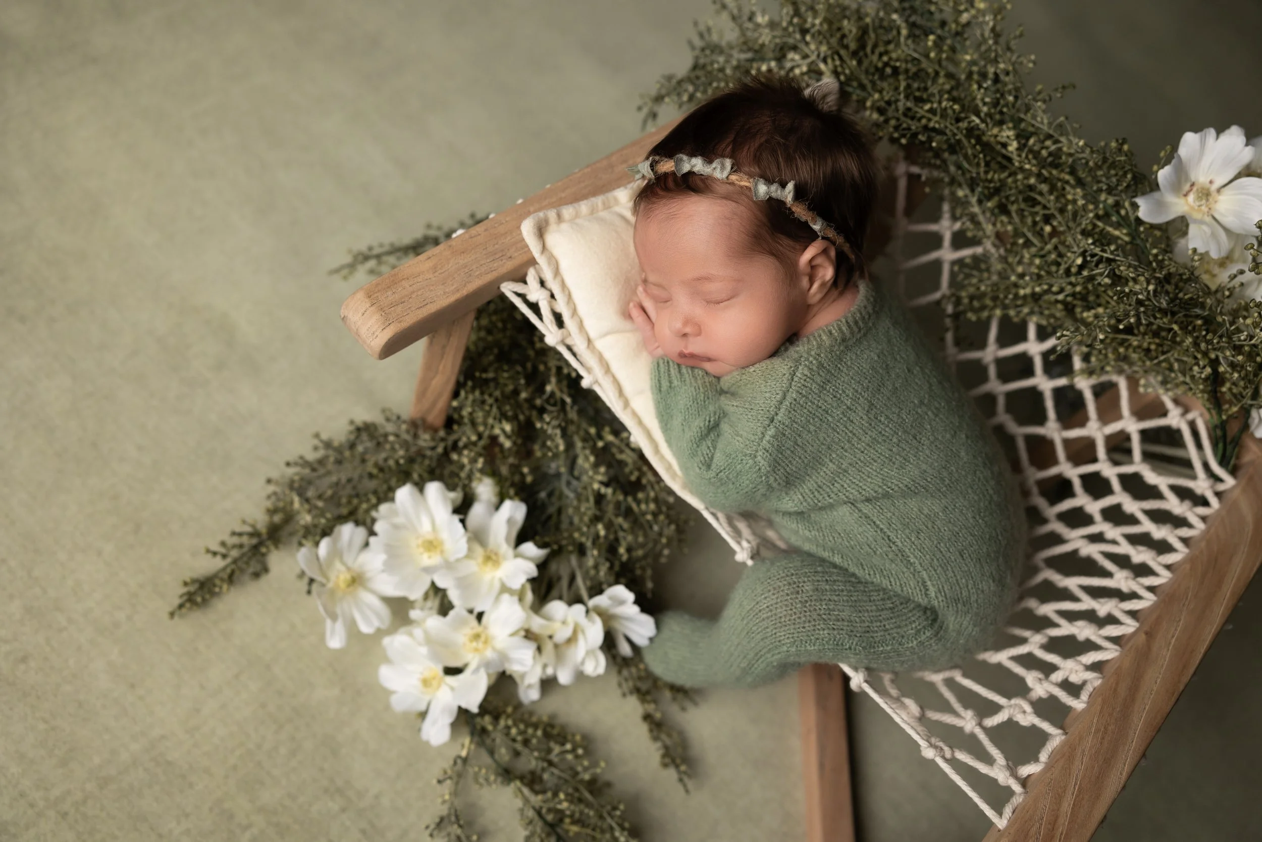 newborn baby in green wrap posed on wooden bed with flowers by austin newborn photographer