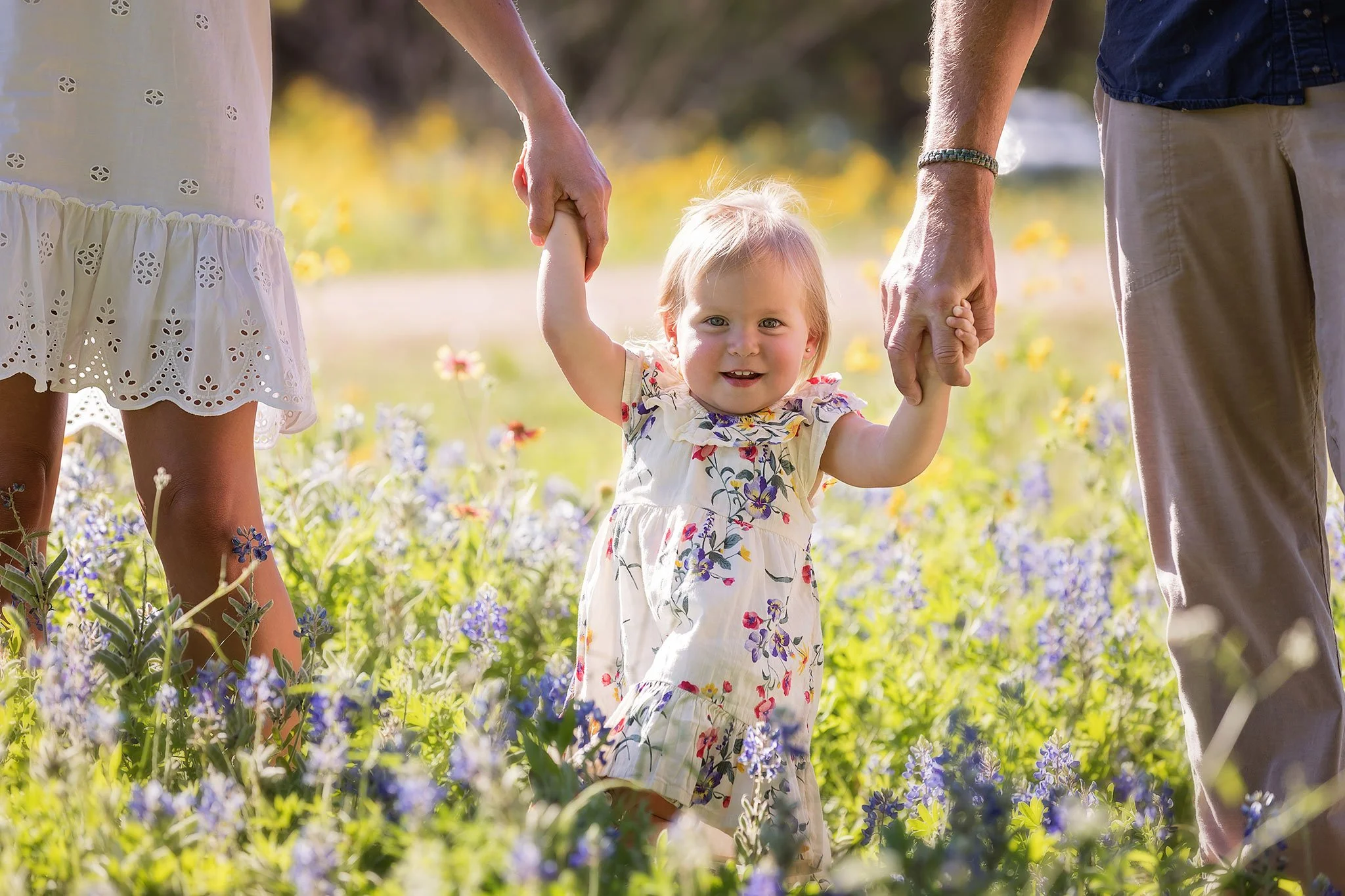 One-year-old baby taking assisted steps through Texas bluebonnets during a milestone photography session in Austin.