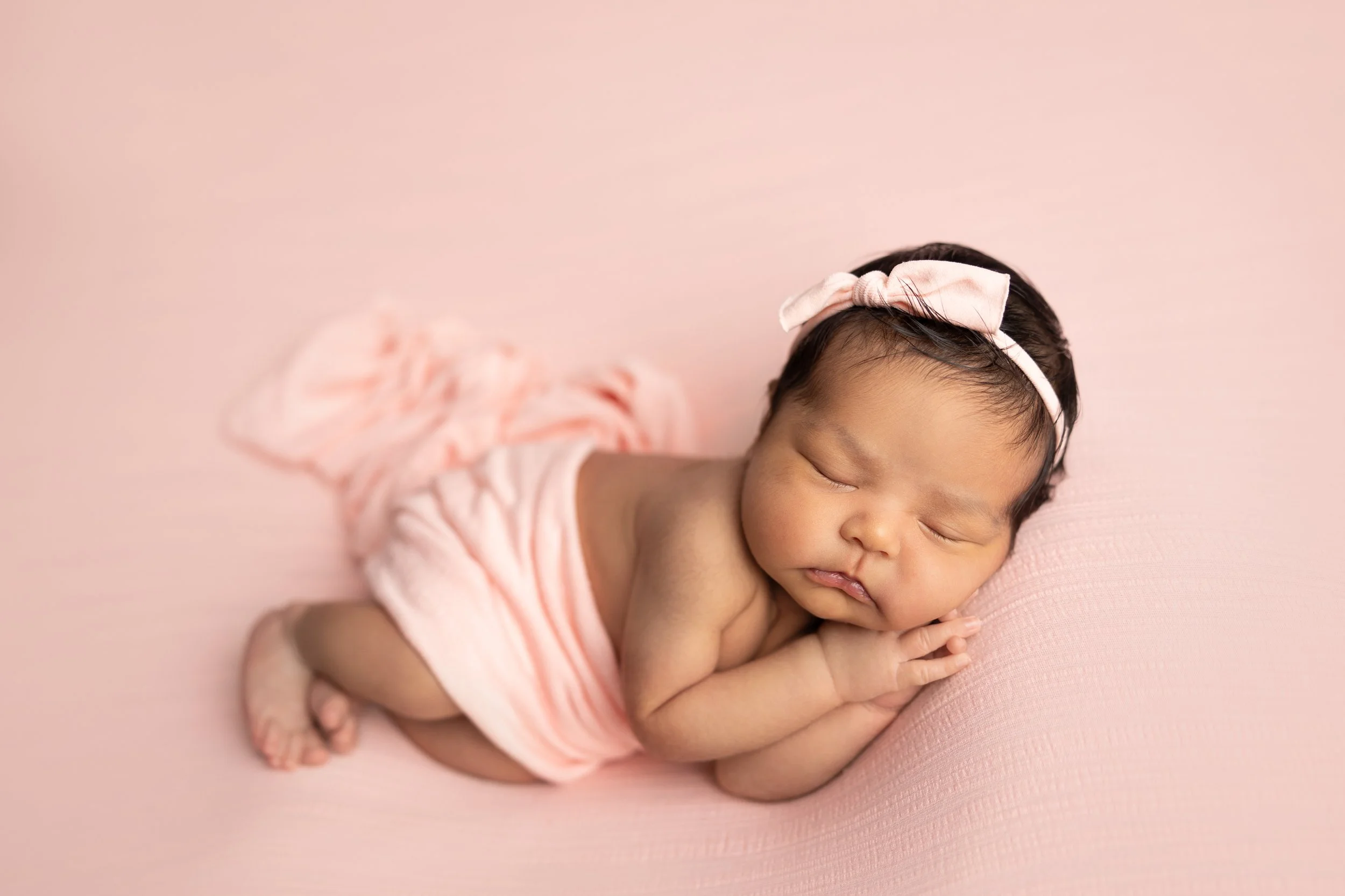 Sleeping newborn baby girl posed on a soft pink backdrop during a studio newborn photography session