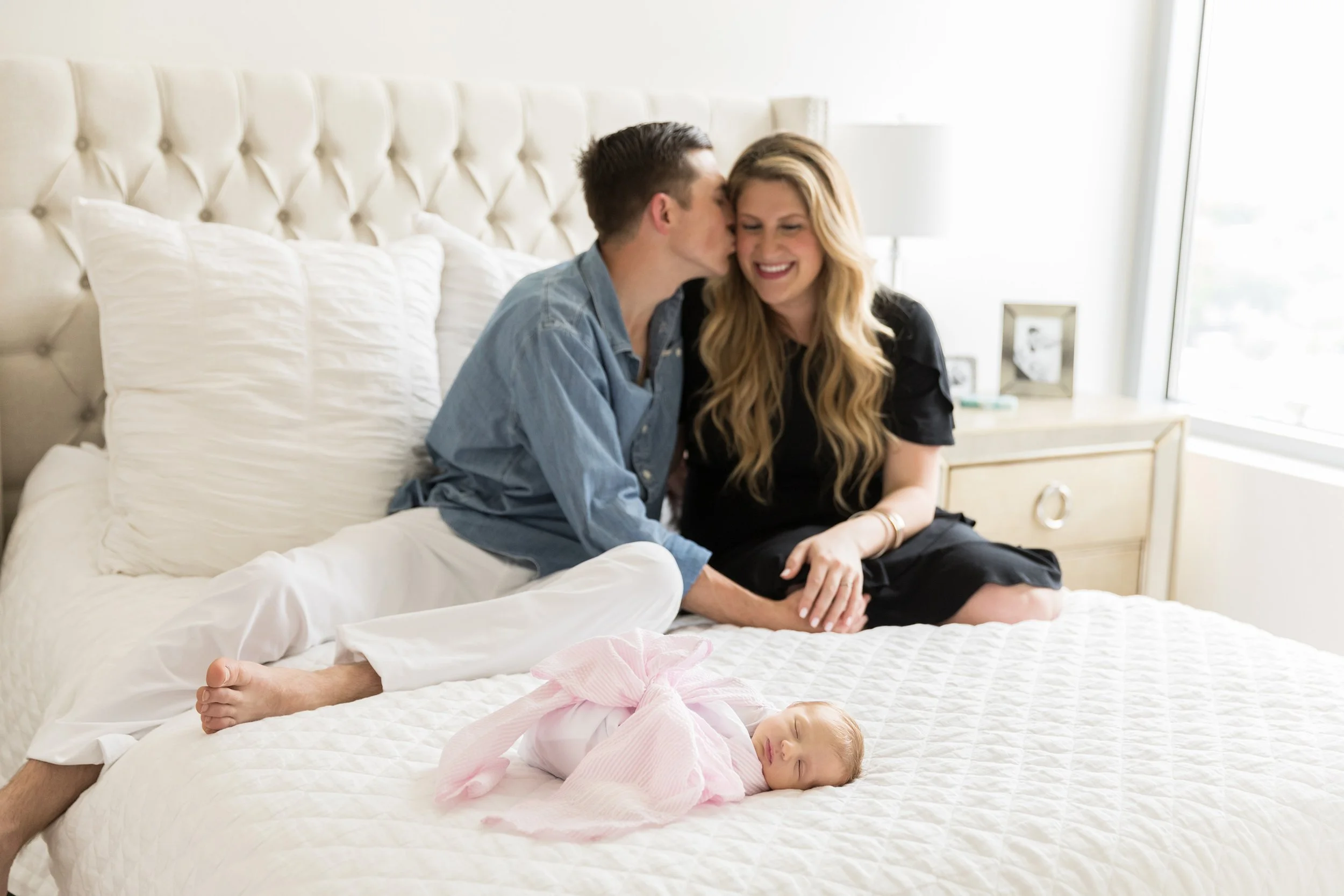 Parents sharing a sweet moment while their newborn rests nearby in the comfort of home.