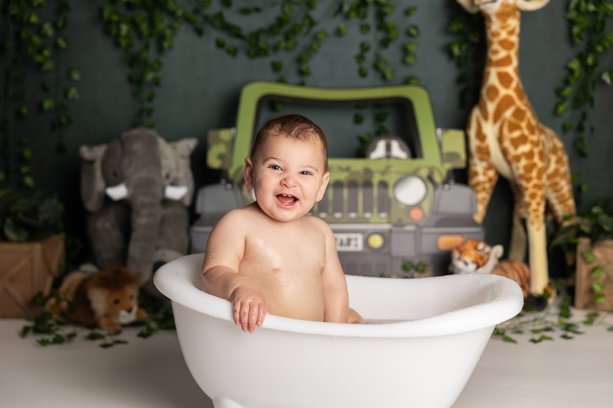 Baby smiling in tub after cake smash session in Austin TX with jungle themed setup