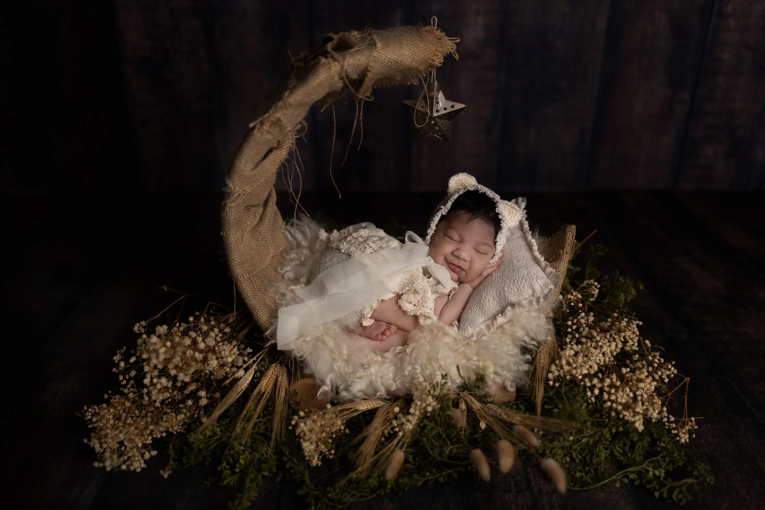 Sleeping smiling newborn baby posed in a moon prop during a studio newborn photography session in Austin, Texas.