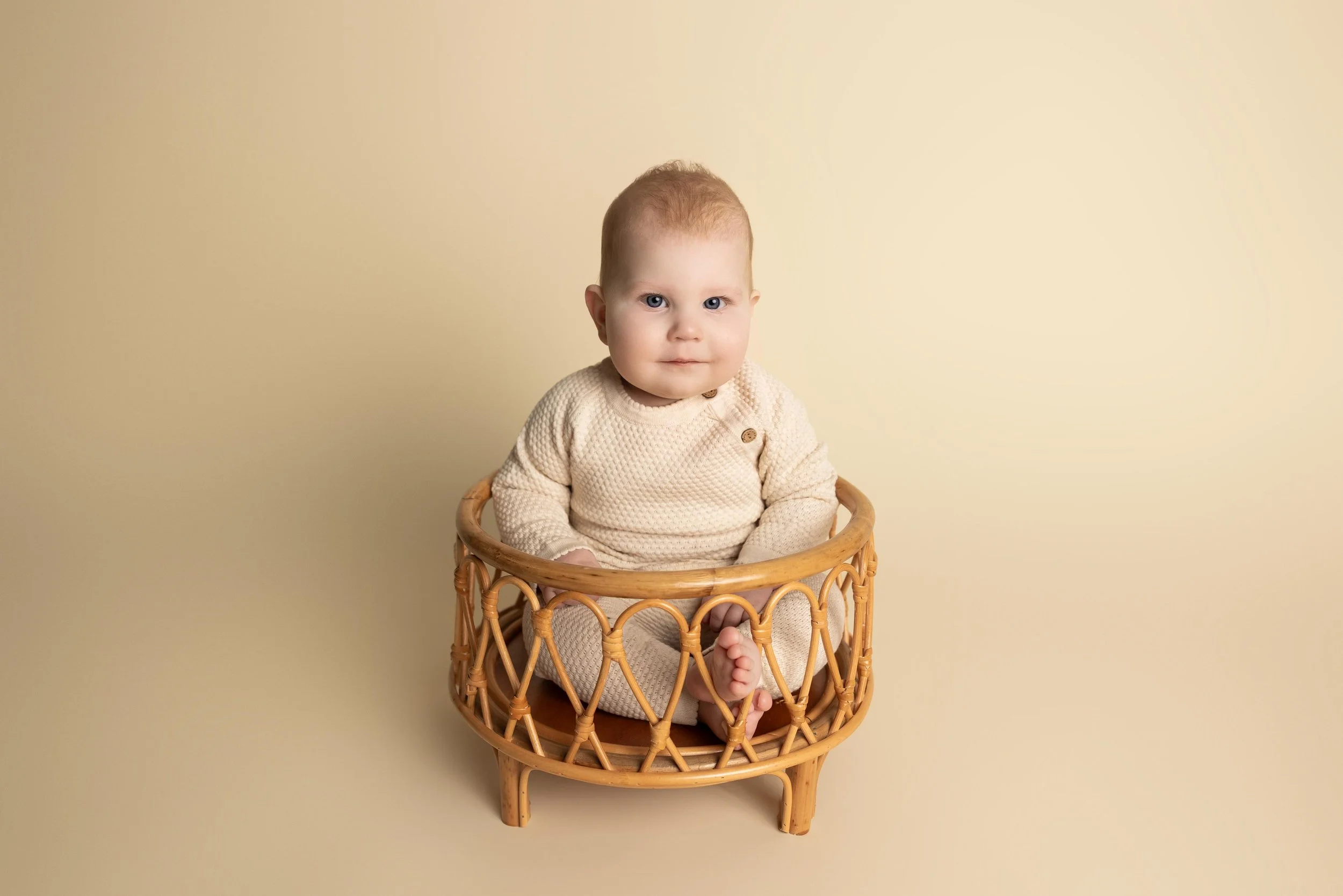 Sitting baby in a wooden basket during an eight-month milestone photography session in Austin.