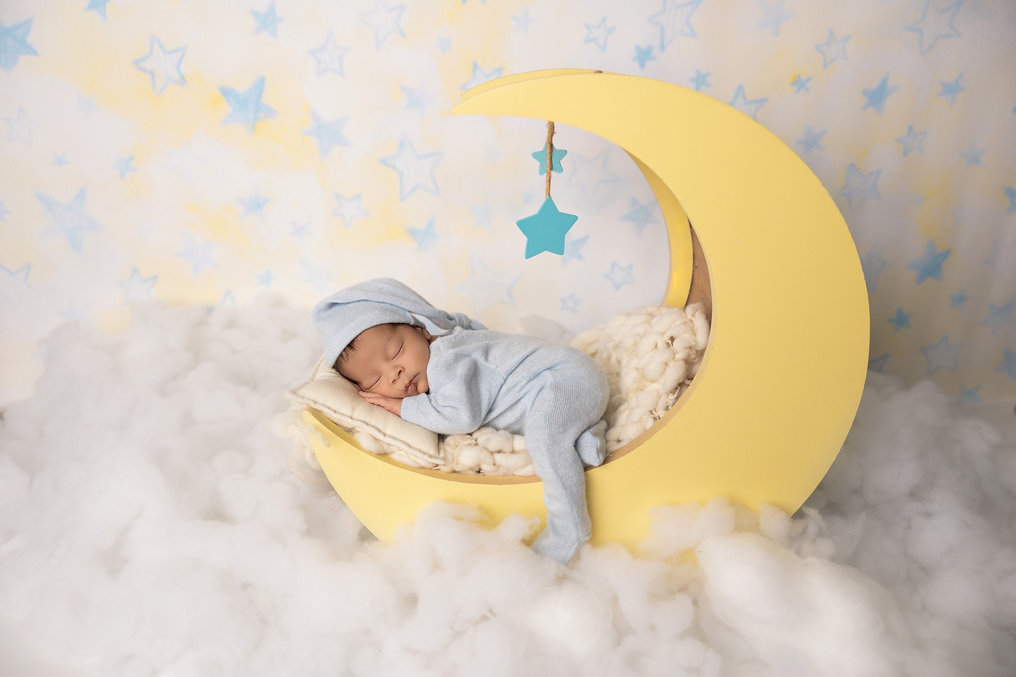 Newborn baby boy posed on moon prop surrounded by clouds and stars