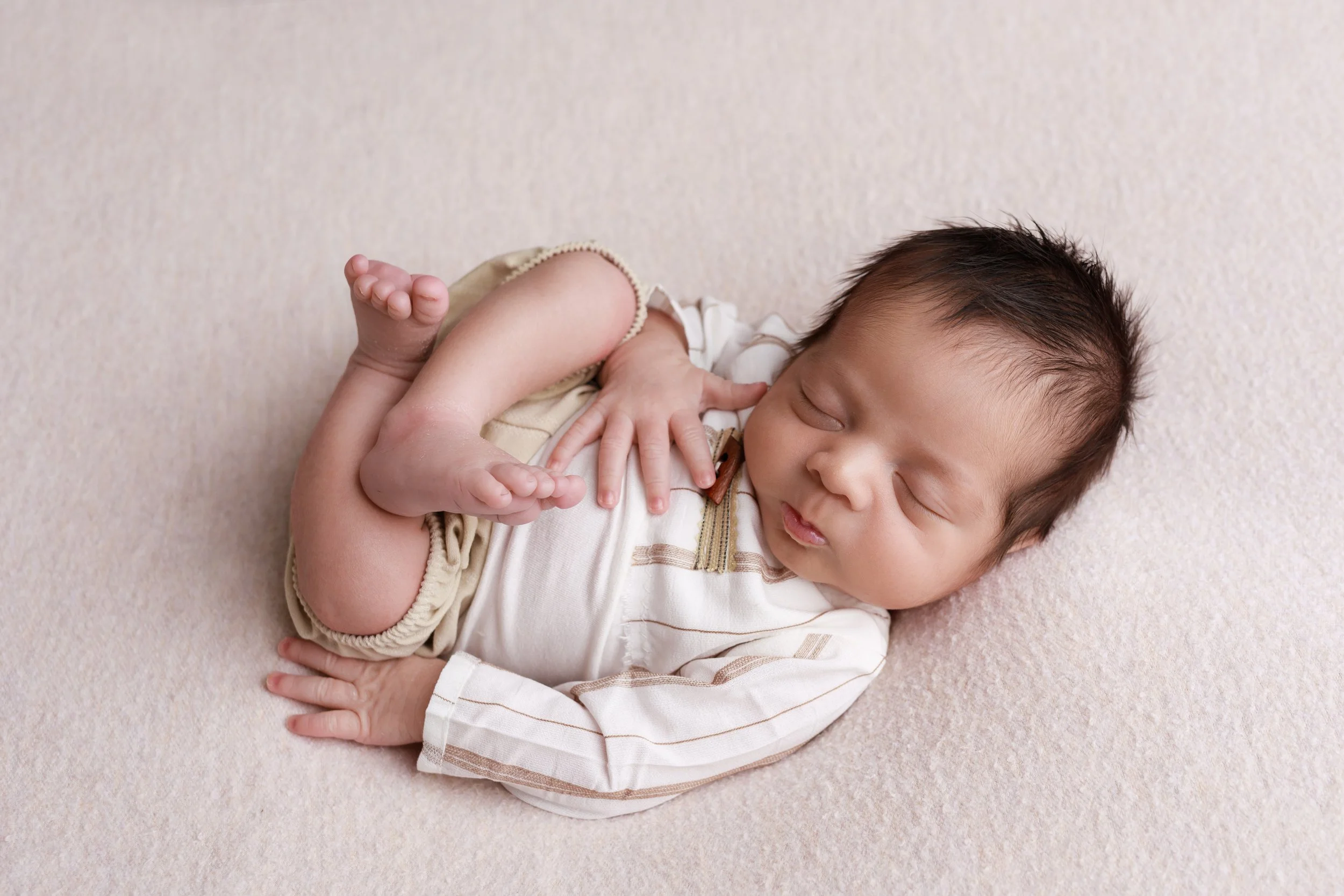 Sleeping newborn baby posed on a cream backdrop during a studio newborn photography session in Austin, Texas..