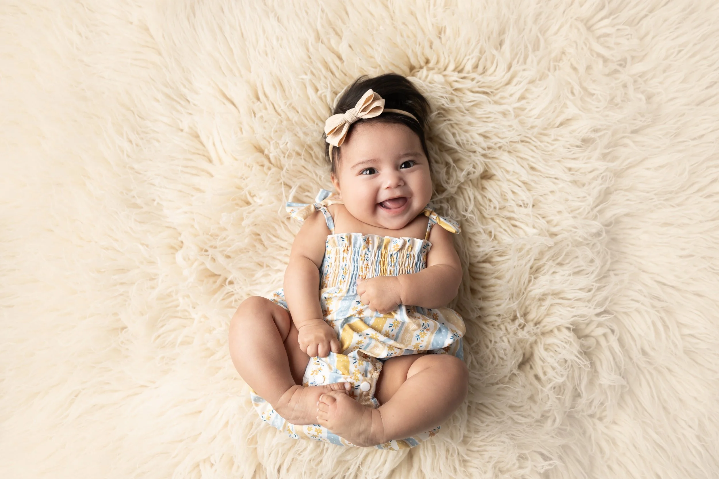 Smiling baby girl lying on a soft cream rug during a milestone photography session at a baby photography studio in Austin, Texas.