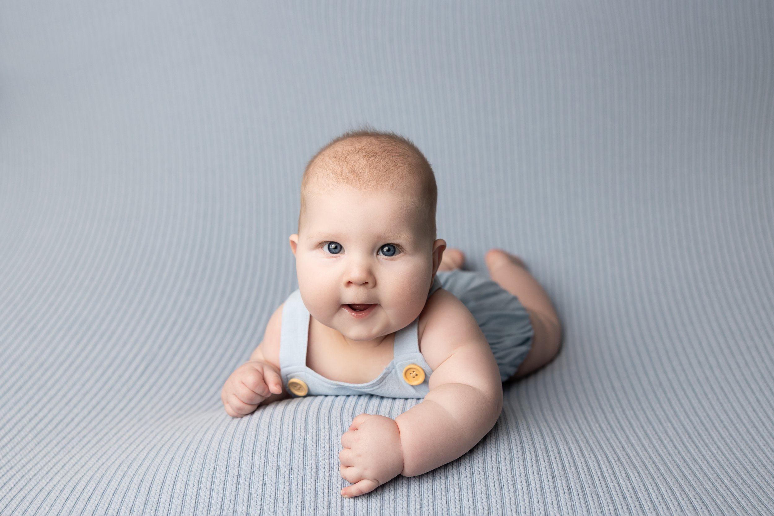 Four-month-old baby smiling during a tummy time milestone photography session in Austin.