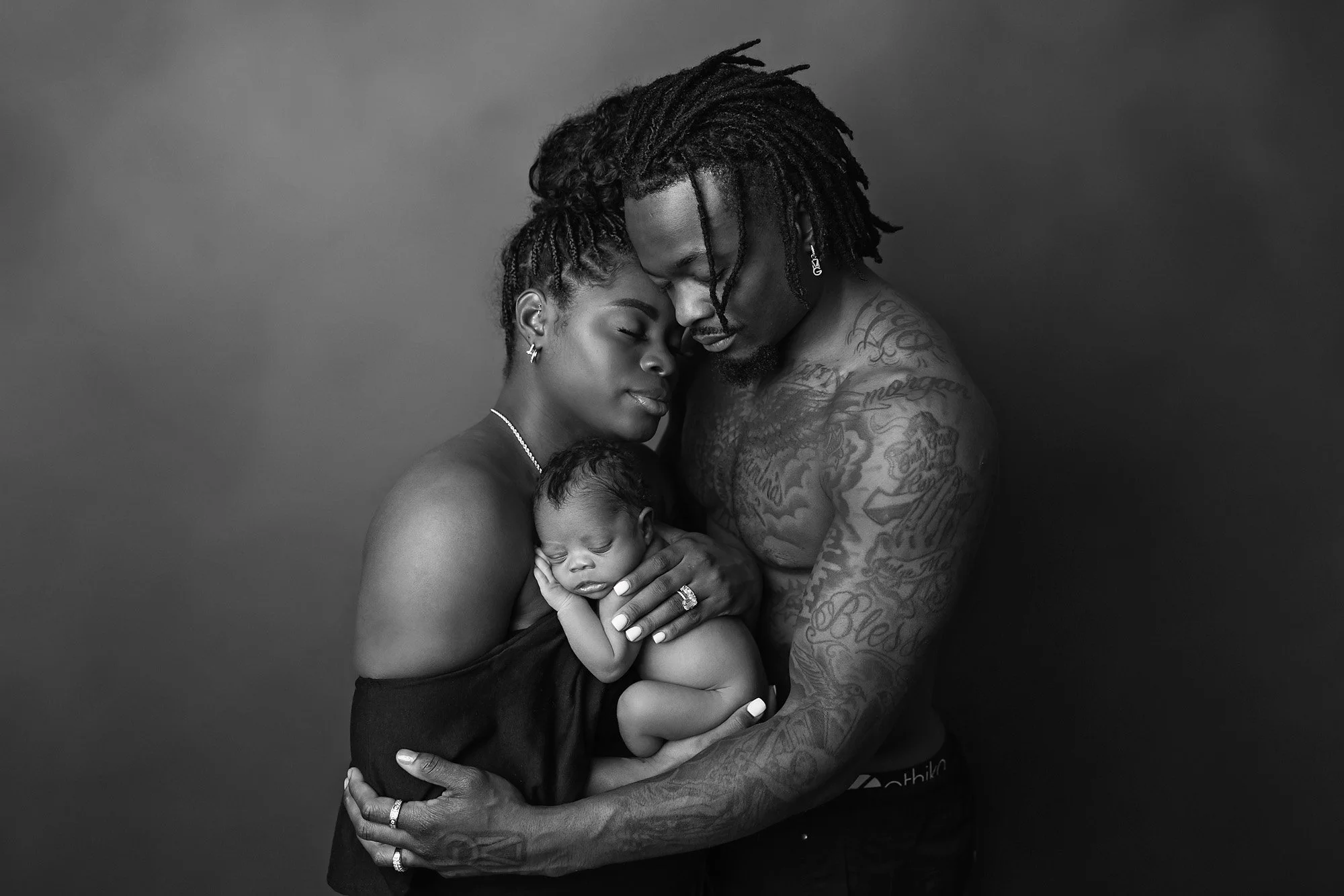 Black and white studio portrait of parents holding their newborn baby skin-to-skin, photographed by an Austin newborn photographer.