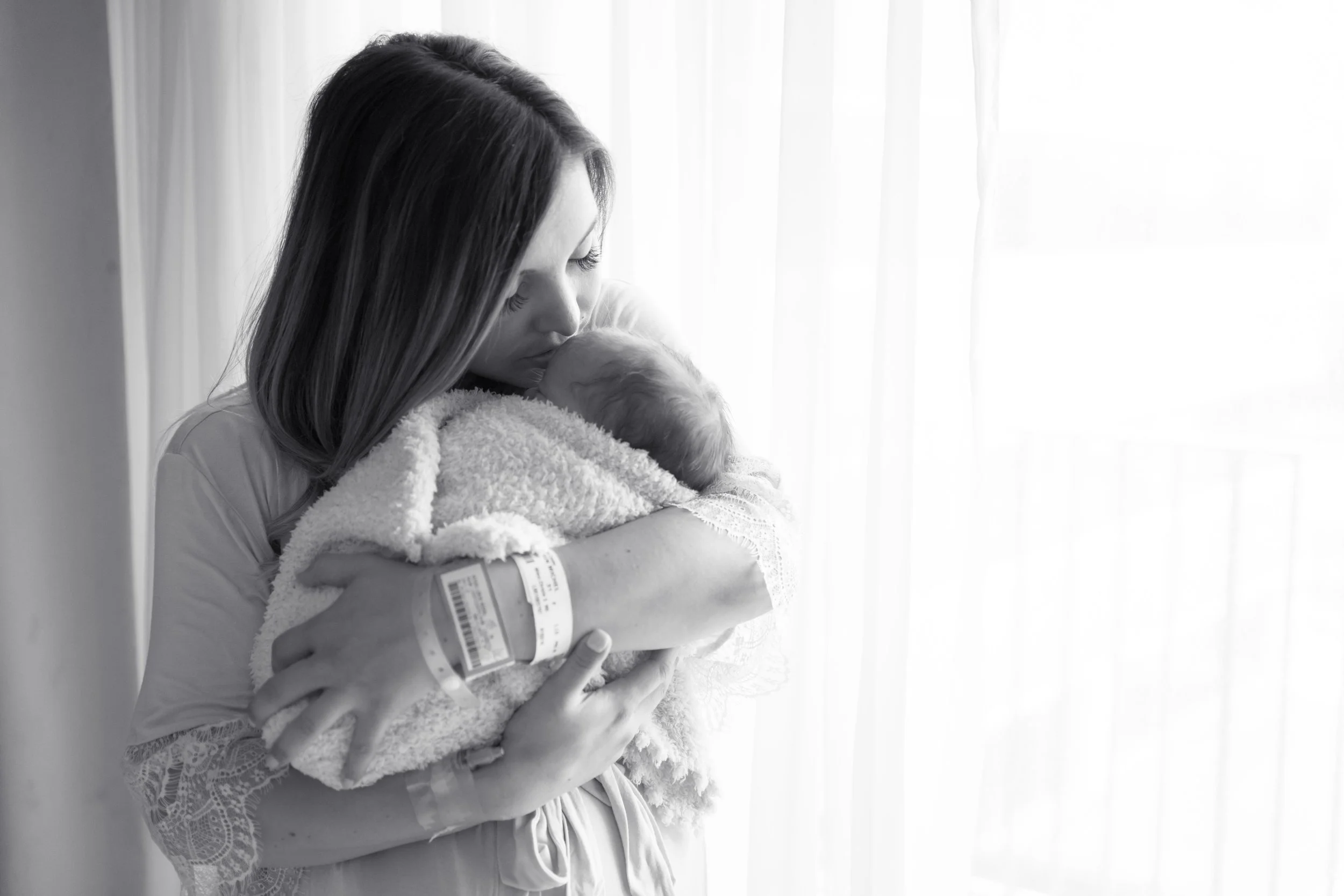 Mother holding her newborn baby near a hospital window during a Fresh 48 photography session in Austin, Texas.