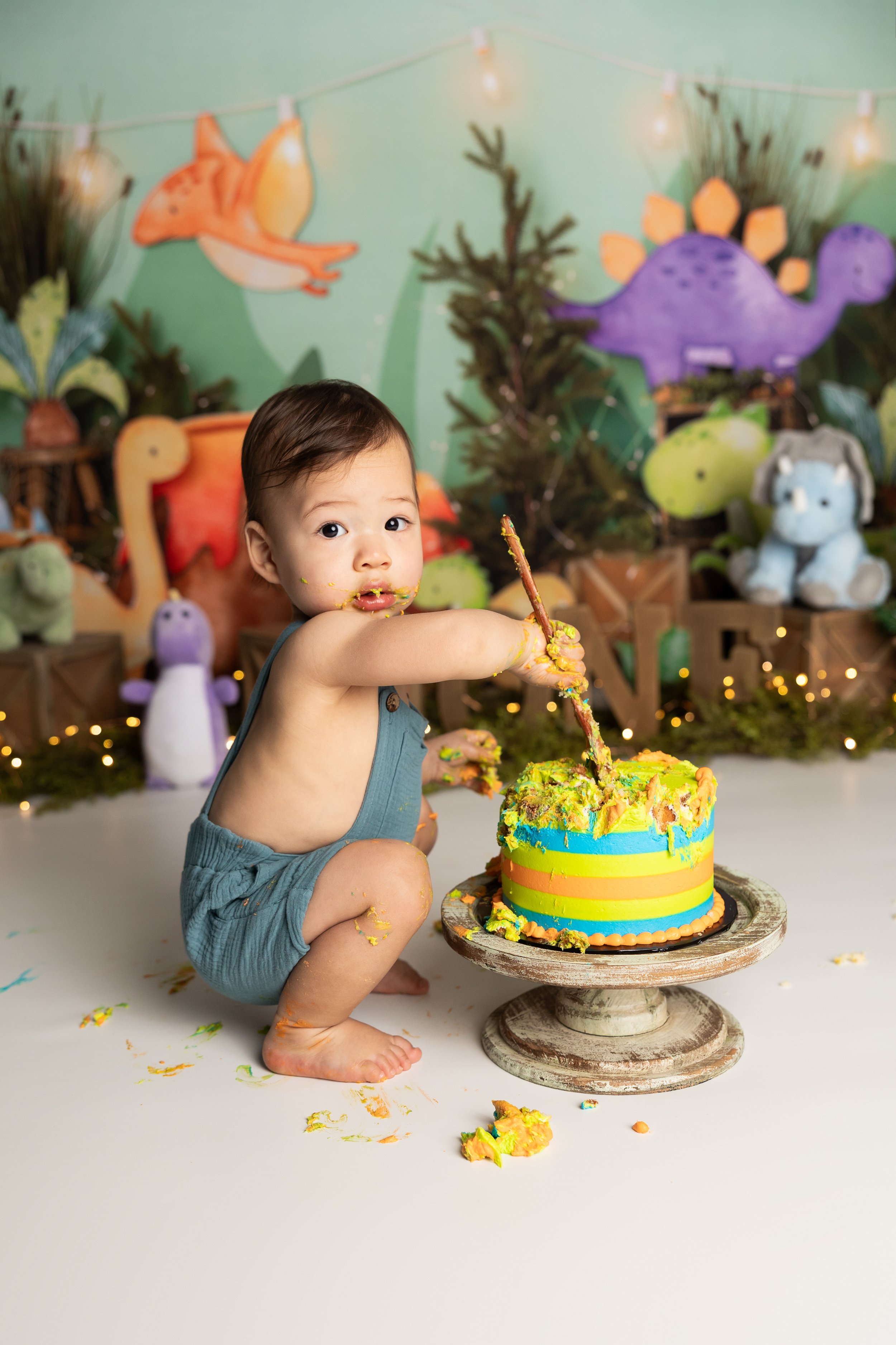 One-year-old boy smashing a colorful birthday cake during a dinosaur-themed first birthday photo session in Austin.
