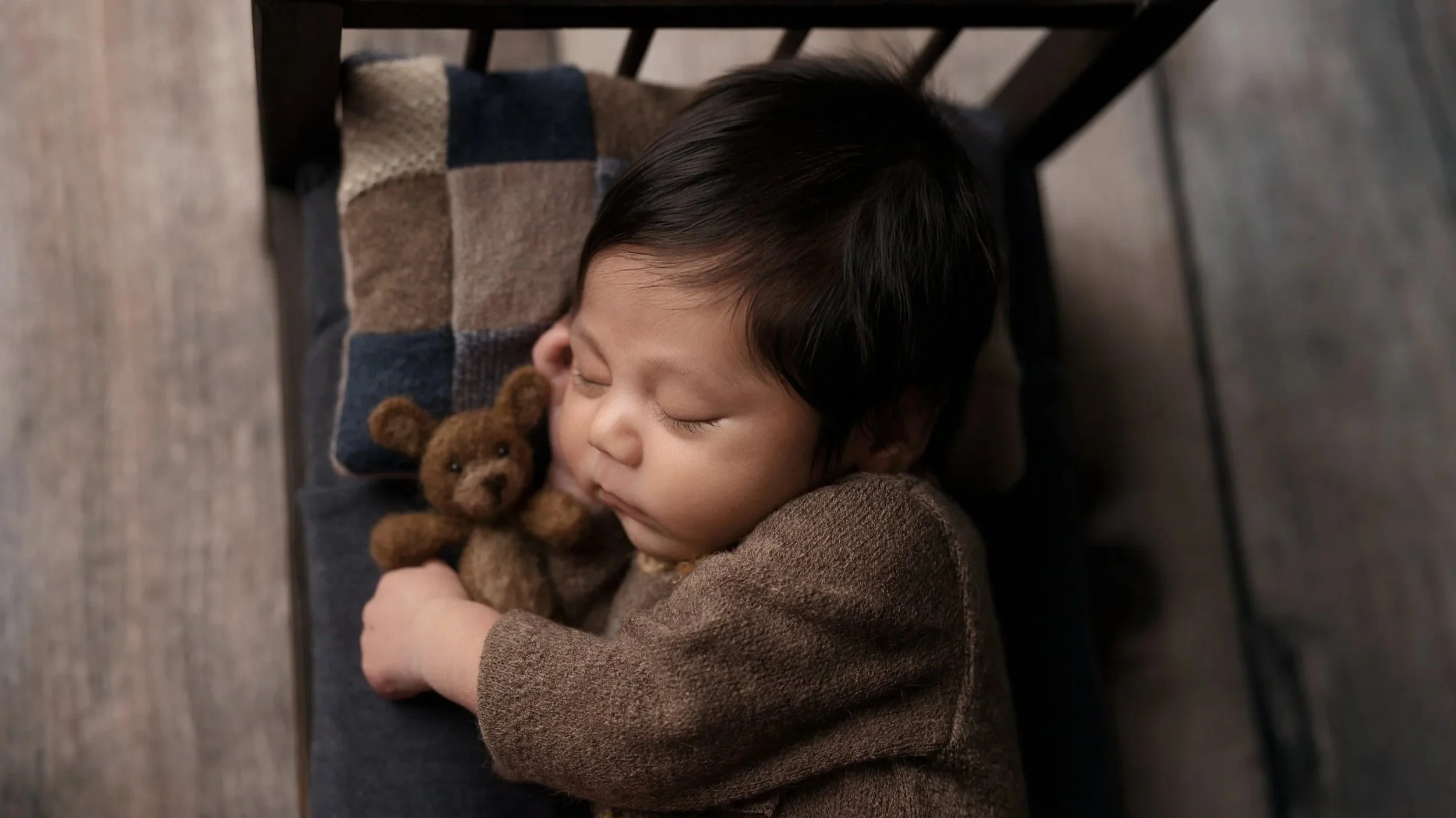 Sleeping newborn baby cuddling a small teddy bear while wearing a soft knit outfit during a cozy studio newborn photography session in Austin, Texas.