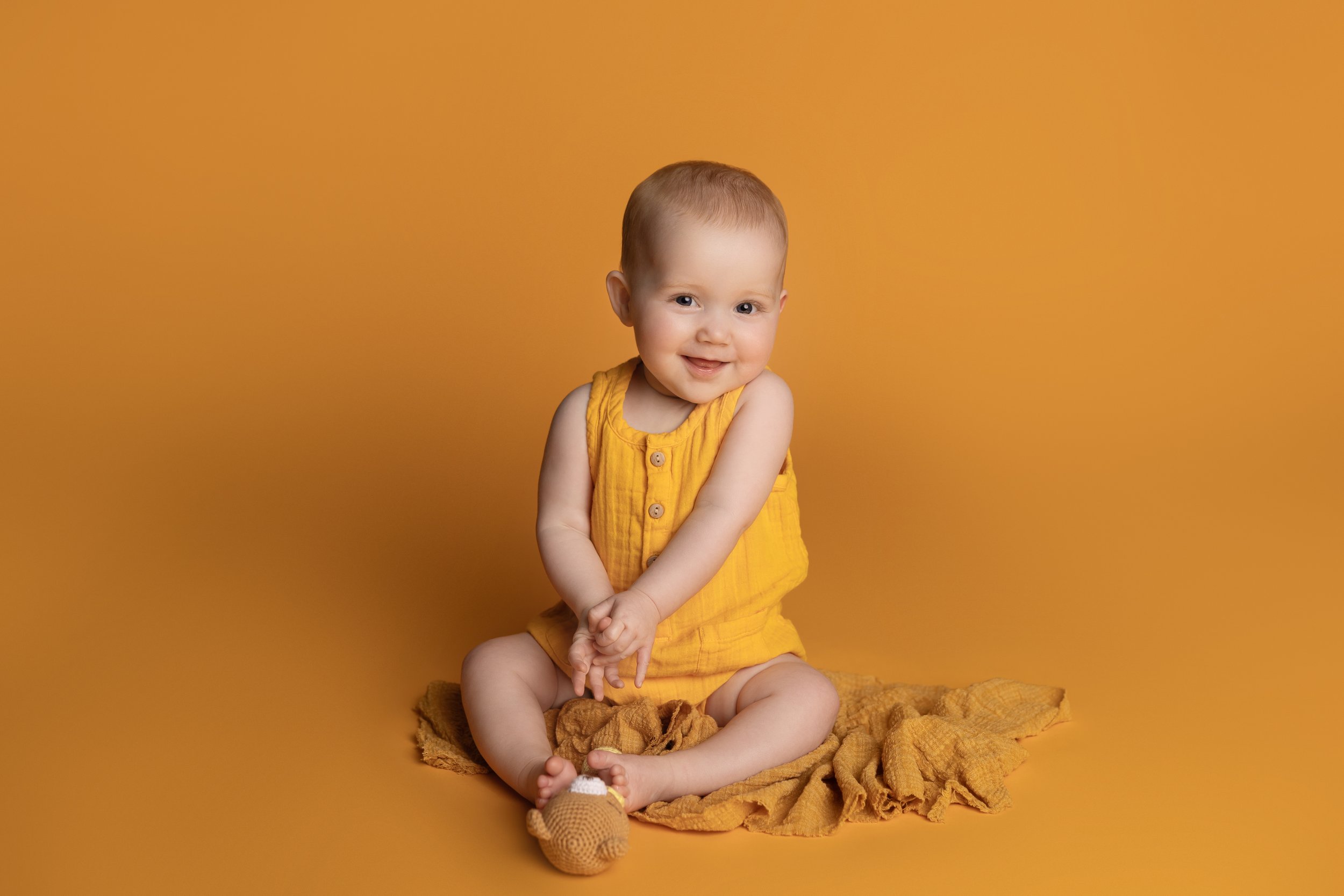 Smiling baby sitting on a dark yellow backdrop during an Austin milestone photography session