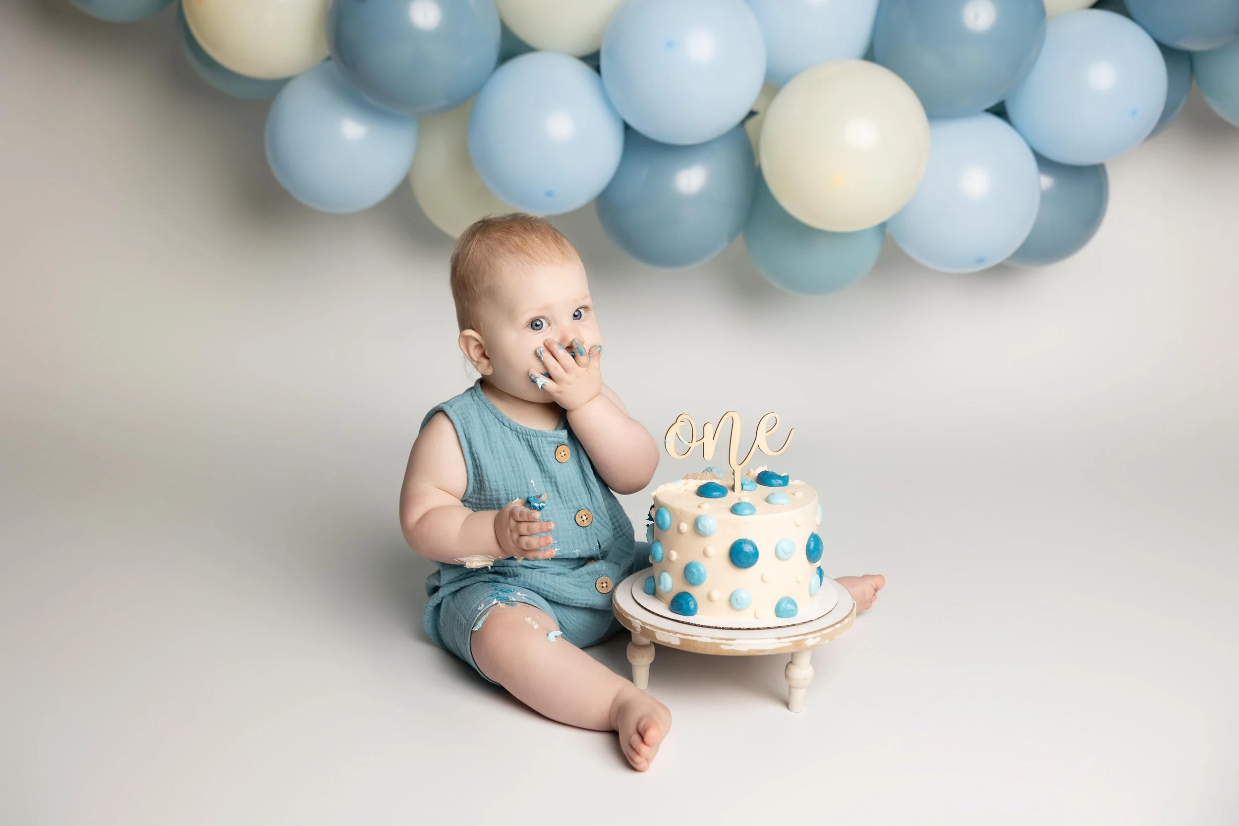 One-year-old baby sitting beside a blue cake during a first birthday cake smash session in Austin.