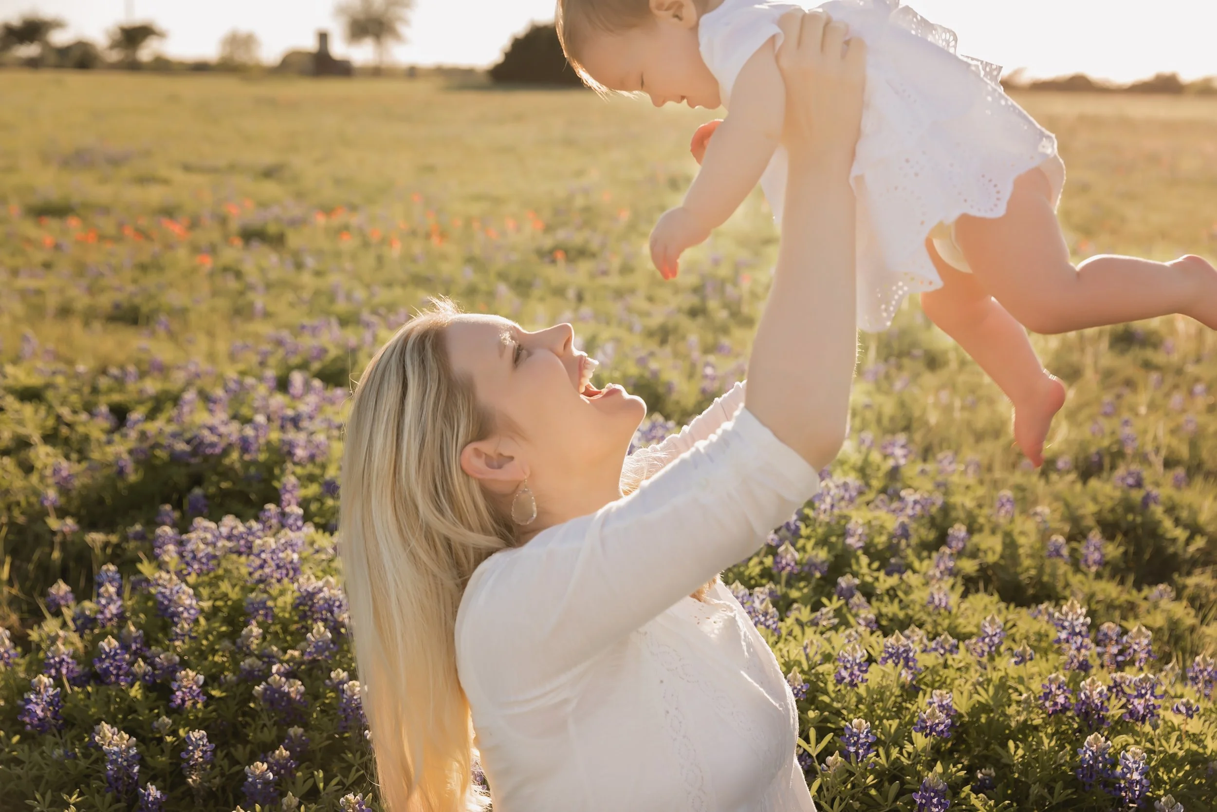 Mom lifting baby girl in a bluebonnet field during golden hour in Austin Texas