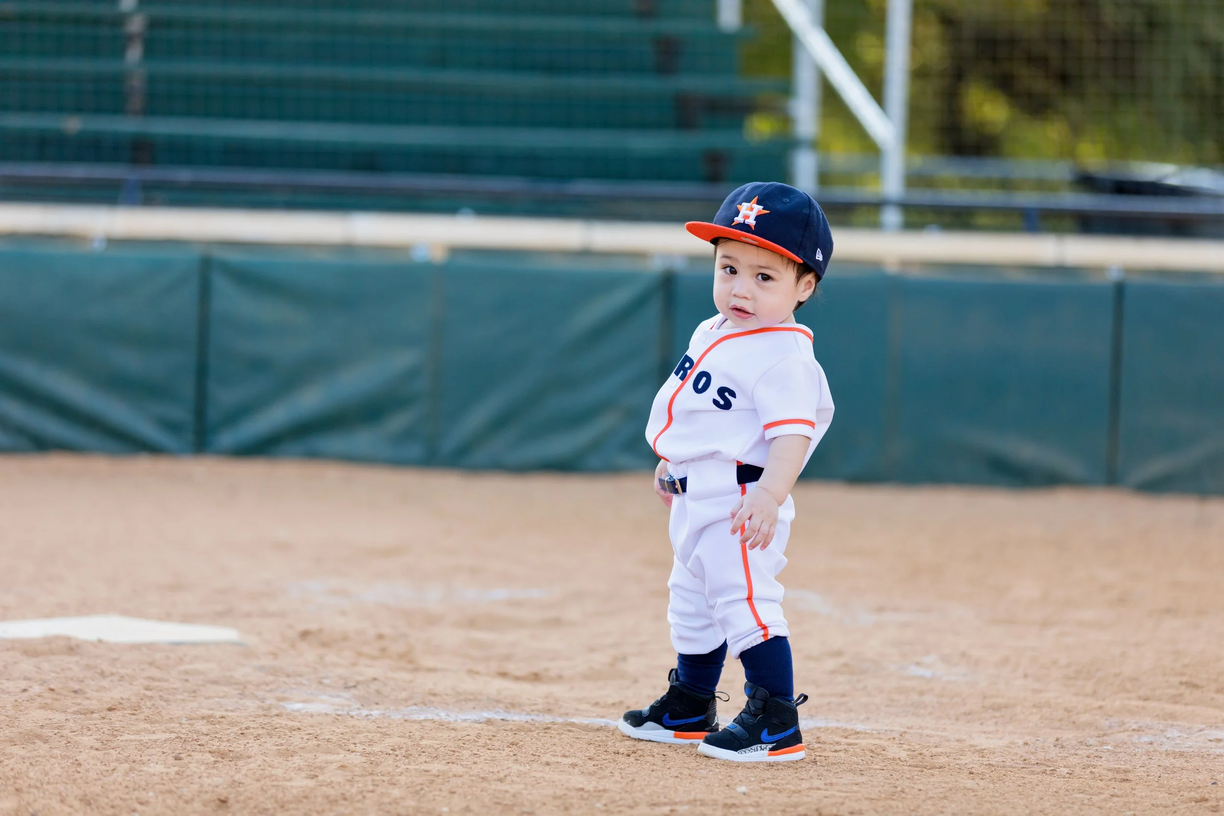 toddler boy standing on baseball field for first birthday photoshoot