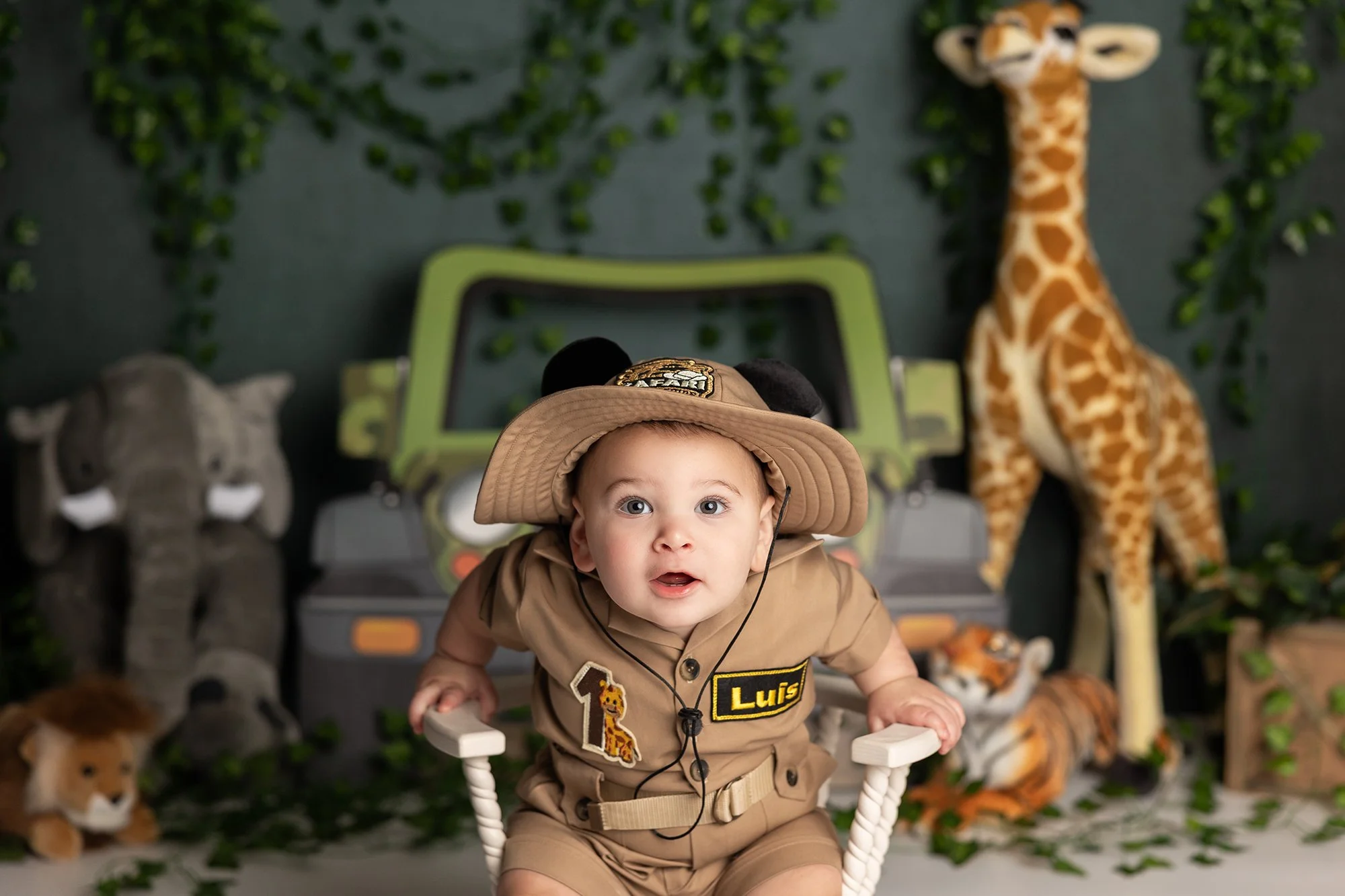 Baby boy in safari outfit during cake smash session in Austin TX with jungle themed backdrop