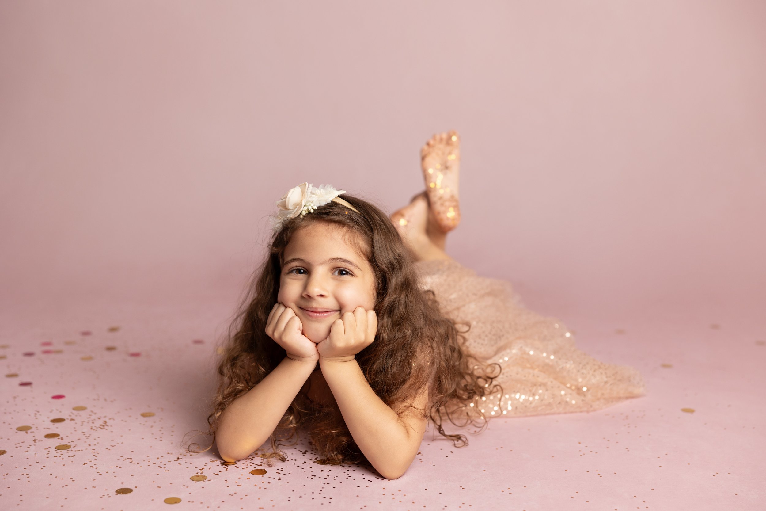Young girl in a sparkly pink dress lying on a pink backdrop with glitter and confetti during an Austin glitter photography session