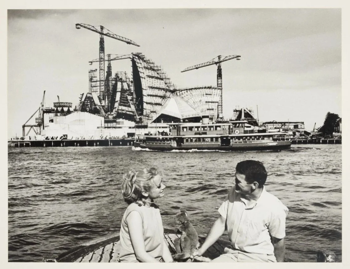 "Couple" (models) with toy kangaroo pose with ferry Lady Ferguson and Opera House under construction]