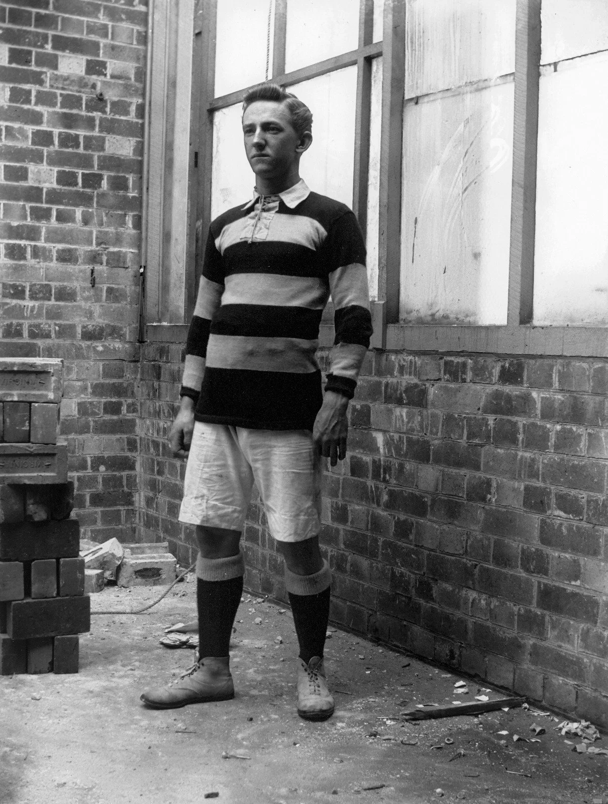 Brisbane football player standing on a building site, ca. 1904