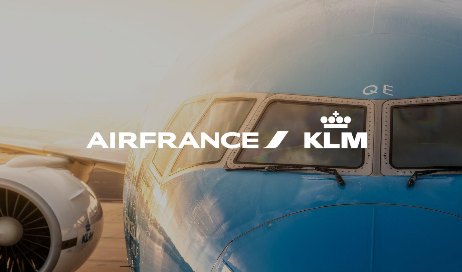 Close-up of an Air France and KLM airplane's cockpit with the airline logos, with a jet engine on the left and a warm sunset glow.