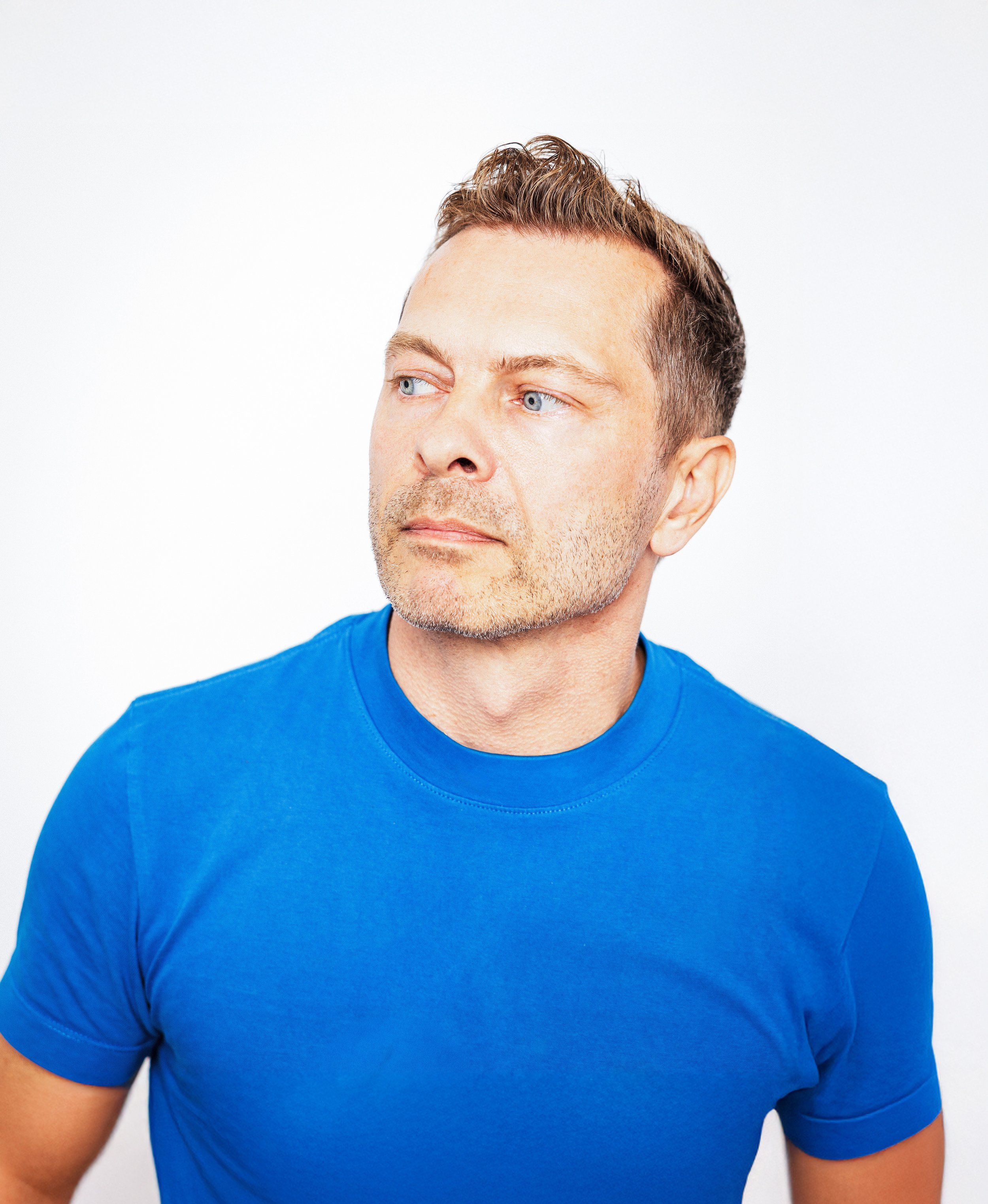 A man wearing a blue shirt looking to the side against a plain white background.