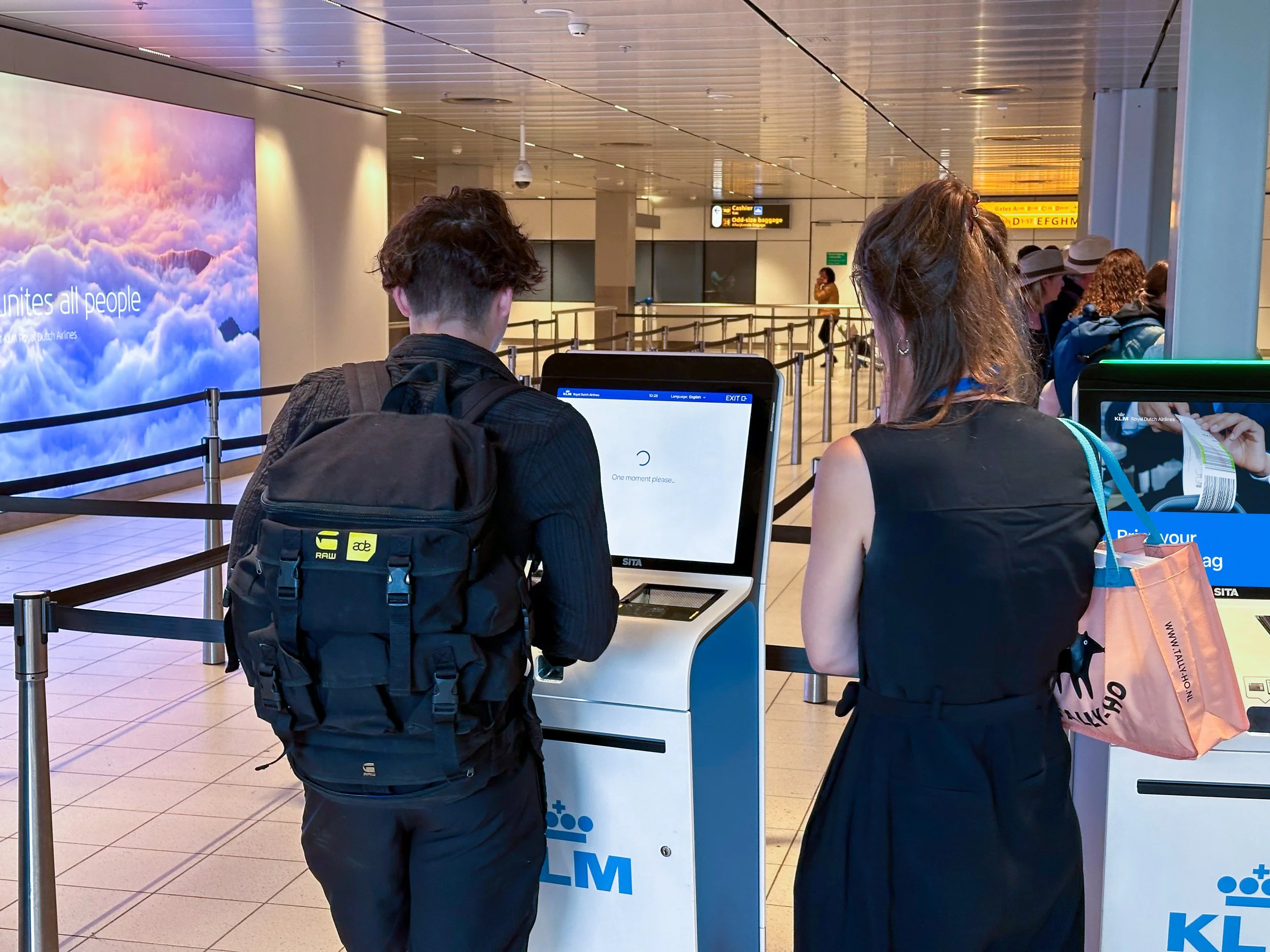 Two passengers using KLM self-service check-in kiosks at Schiphol Airport
