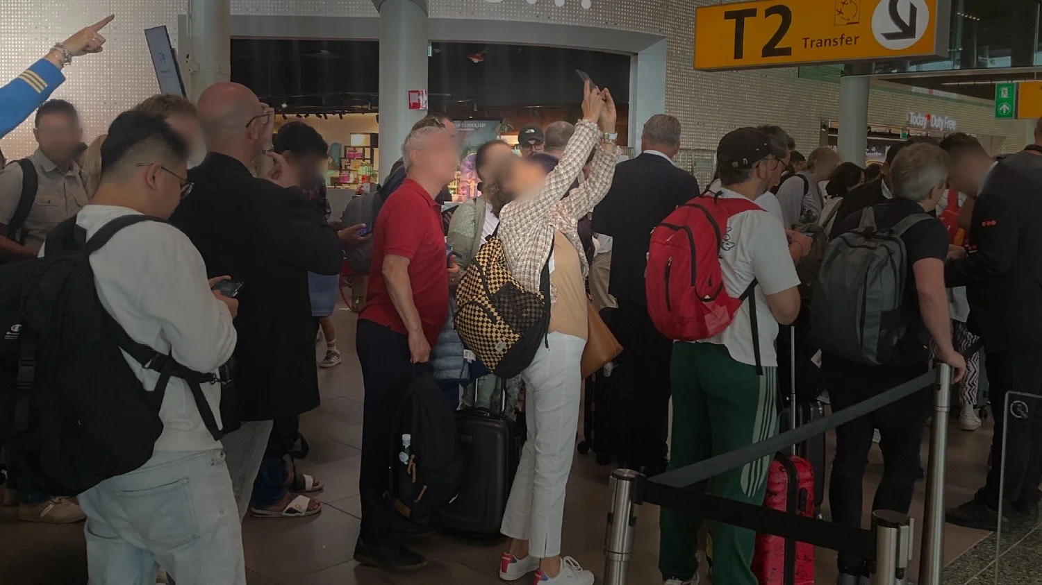 Crowded Transfer Centre at Schiphol Airport during flight disruptions, showing passengers waiting for rebooking assistance