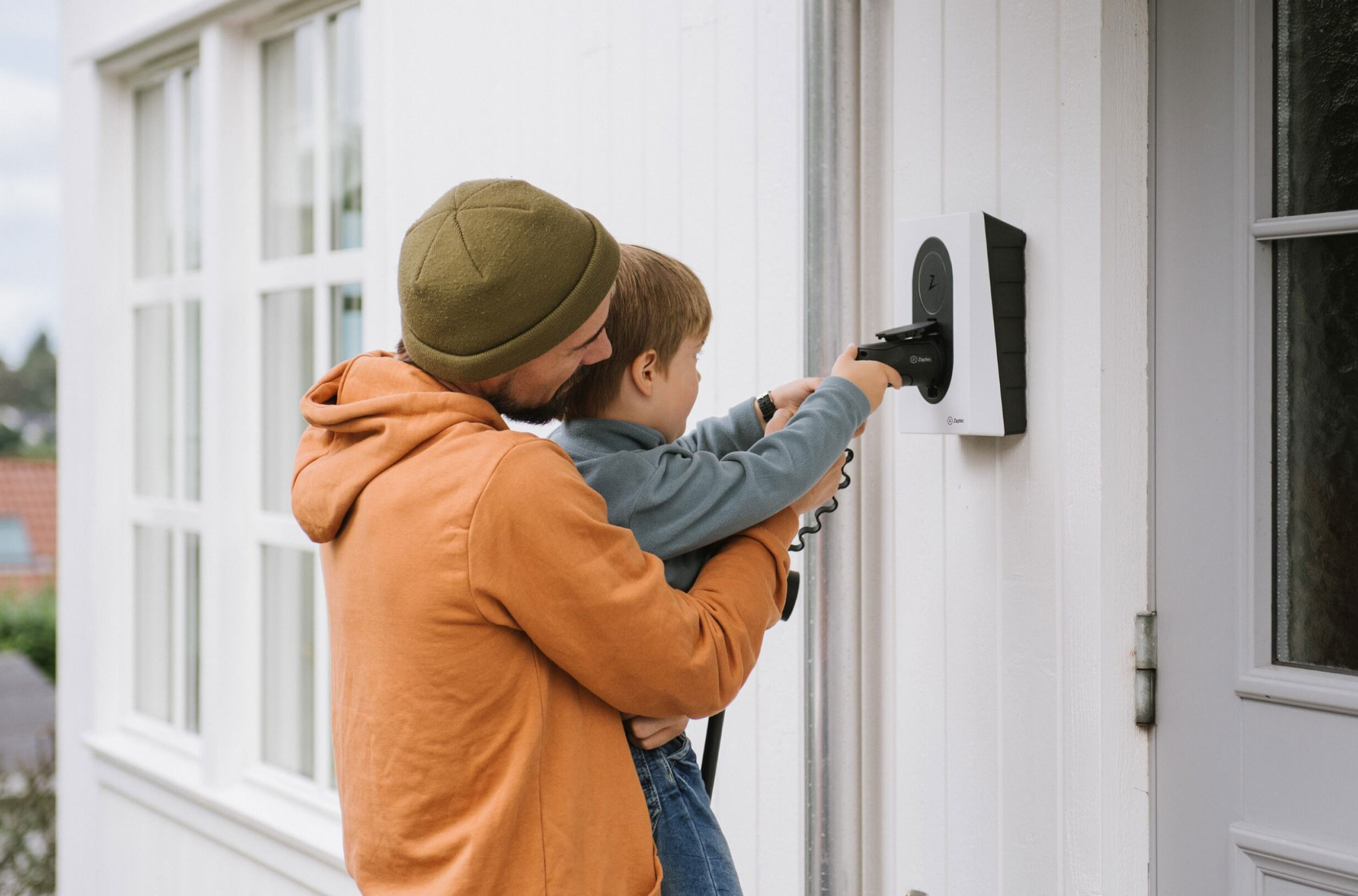 Father and child interacting with a home EV charger mounted on an exterior wall
