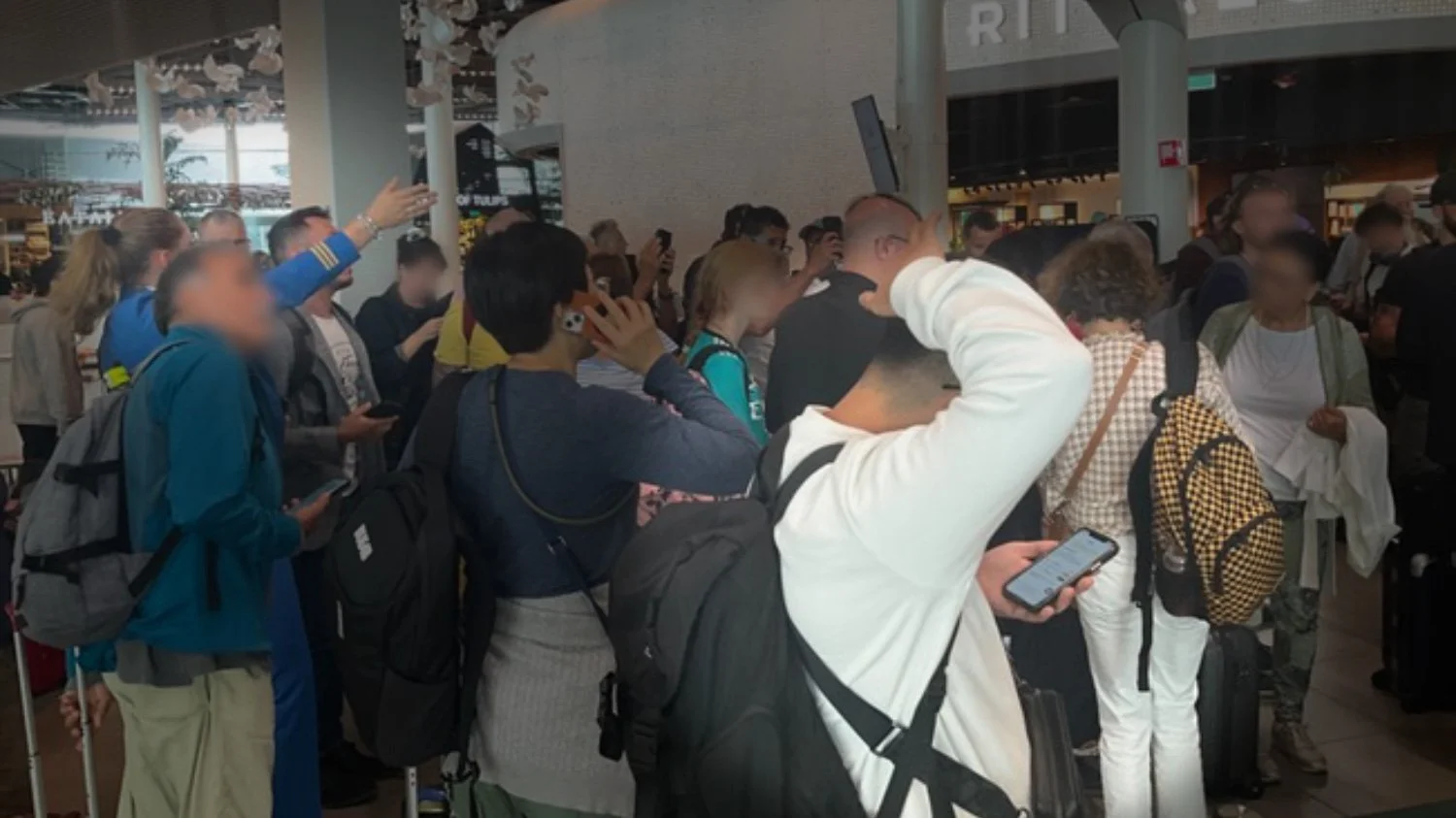 Crowded Transfer Centre at Schiphol Airport during flight disruptions, showing passengers waiting for rebooking assistance