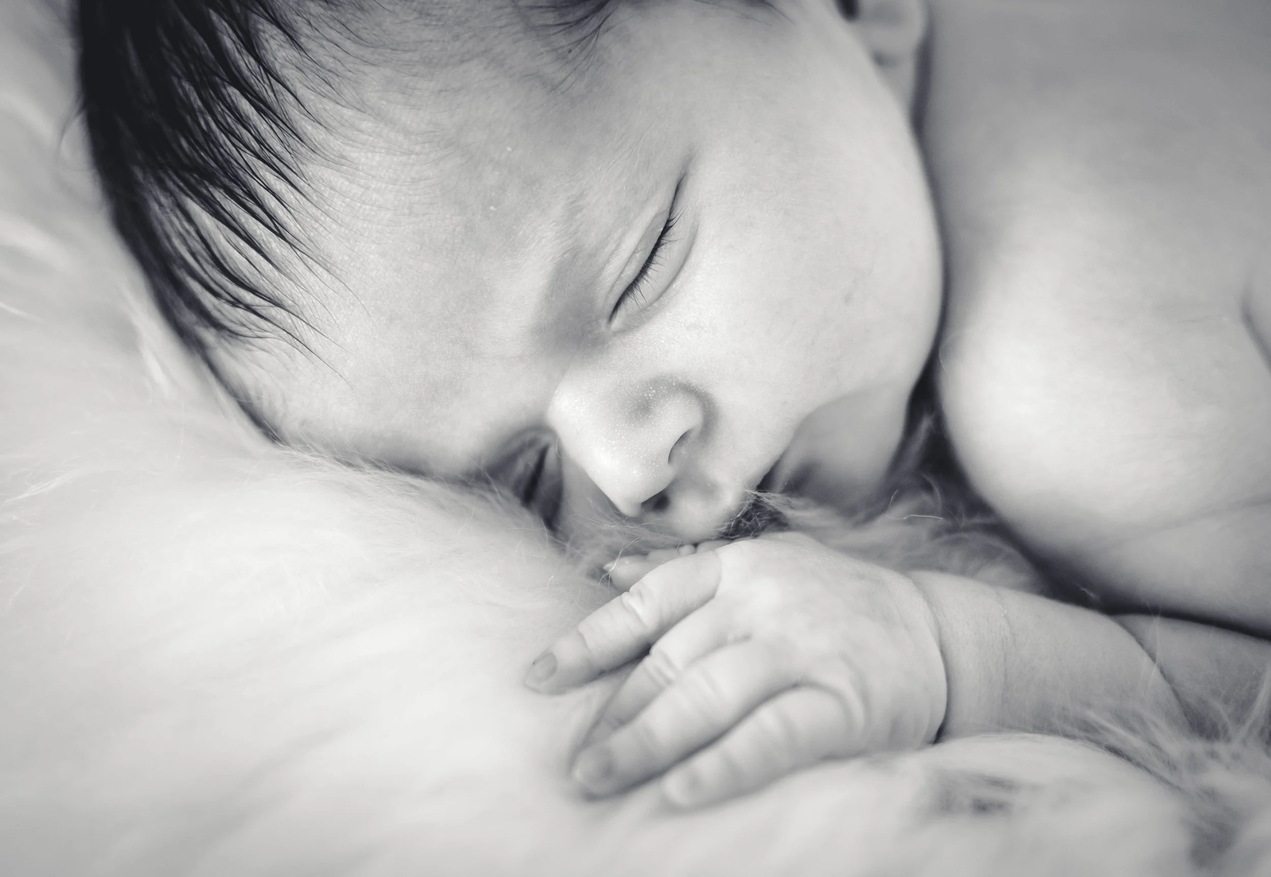 Close-up van een slapende baby met gesloten ogen, met een hand die zachtjes een arm of zijde vasthoudt.