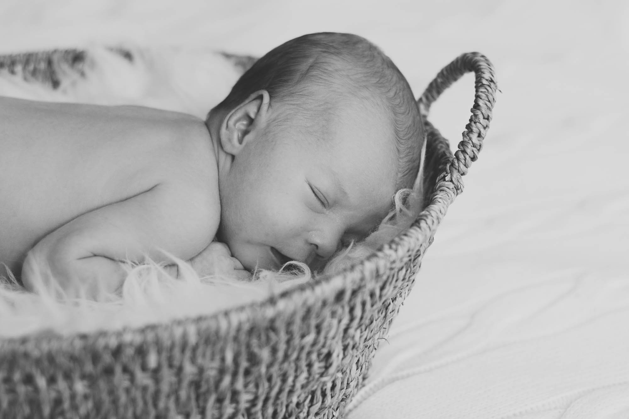 Zacht zwart-witbeeld van een slapende baby in een wollen mand, omgeven door zachte dekens.
