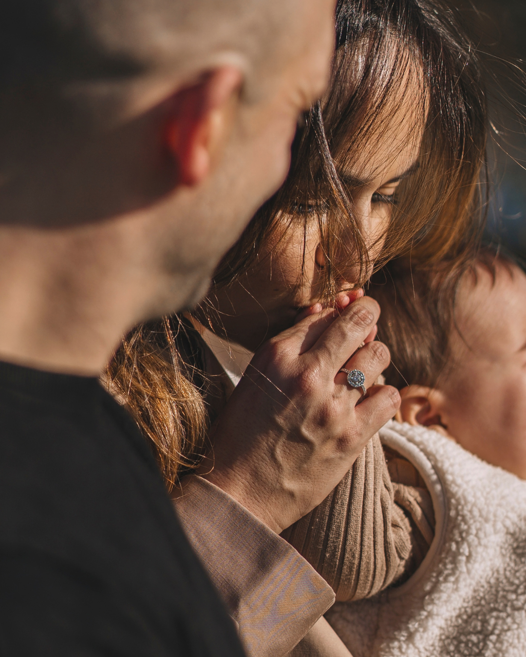 Een close-up van een vrouw die haar hand met een ring op haar lip legt, terwijl een man naast haar kijkt. De vrouw heeft bruin haar en draagt een ring met een grote steen.