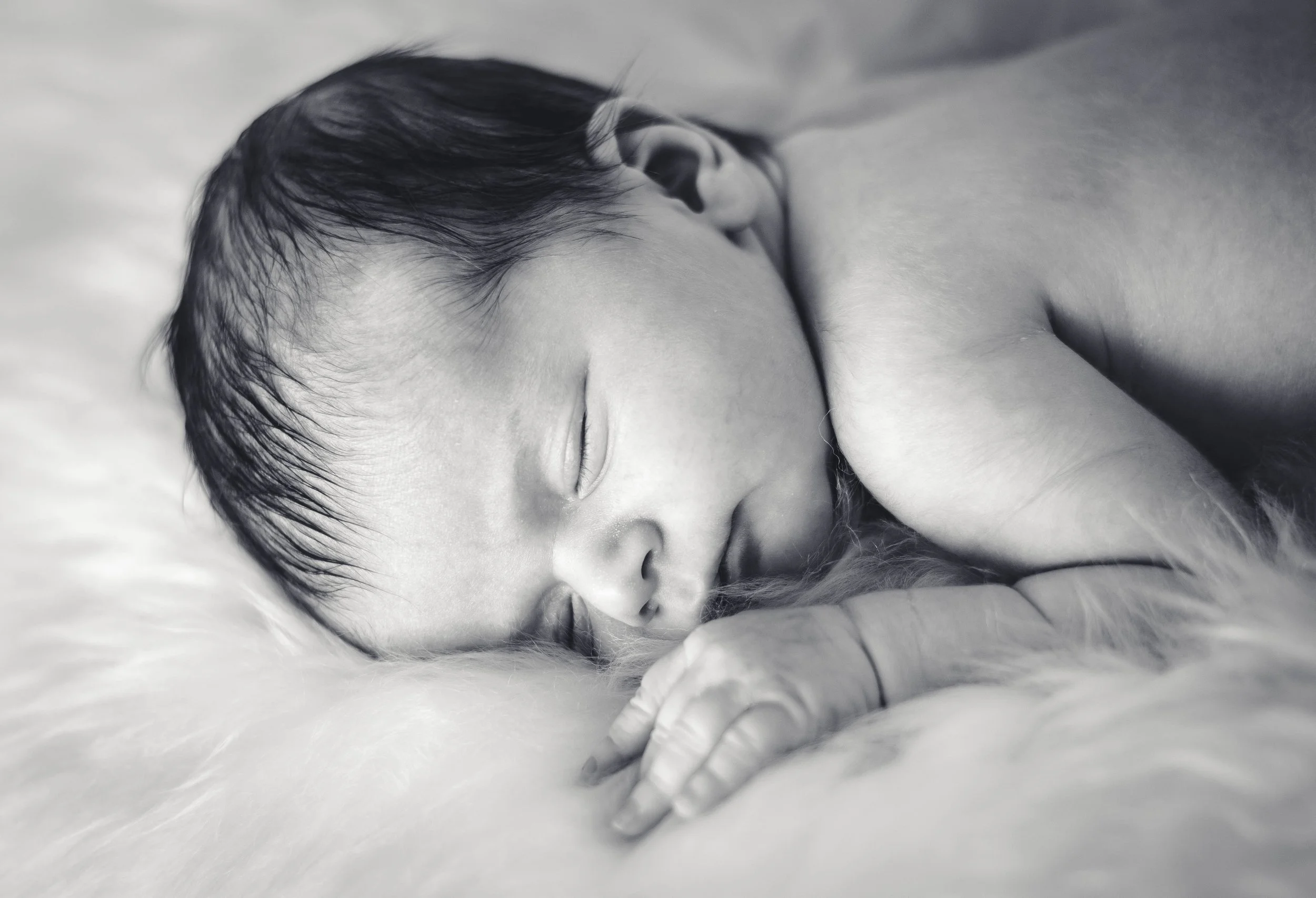 Een slapende baby met donker haar die op een zachte, witte deken ligt.