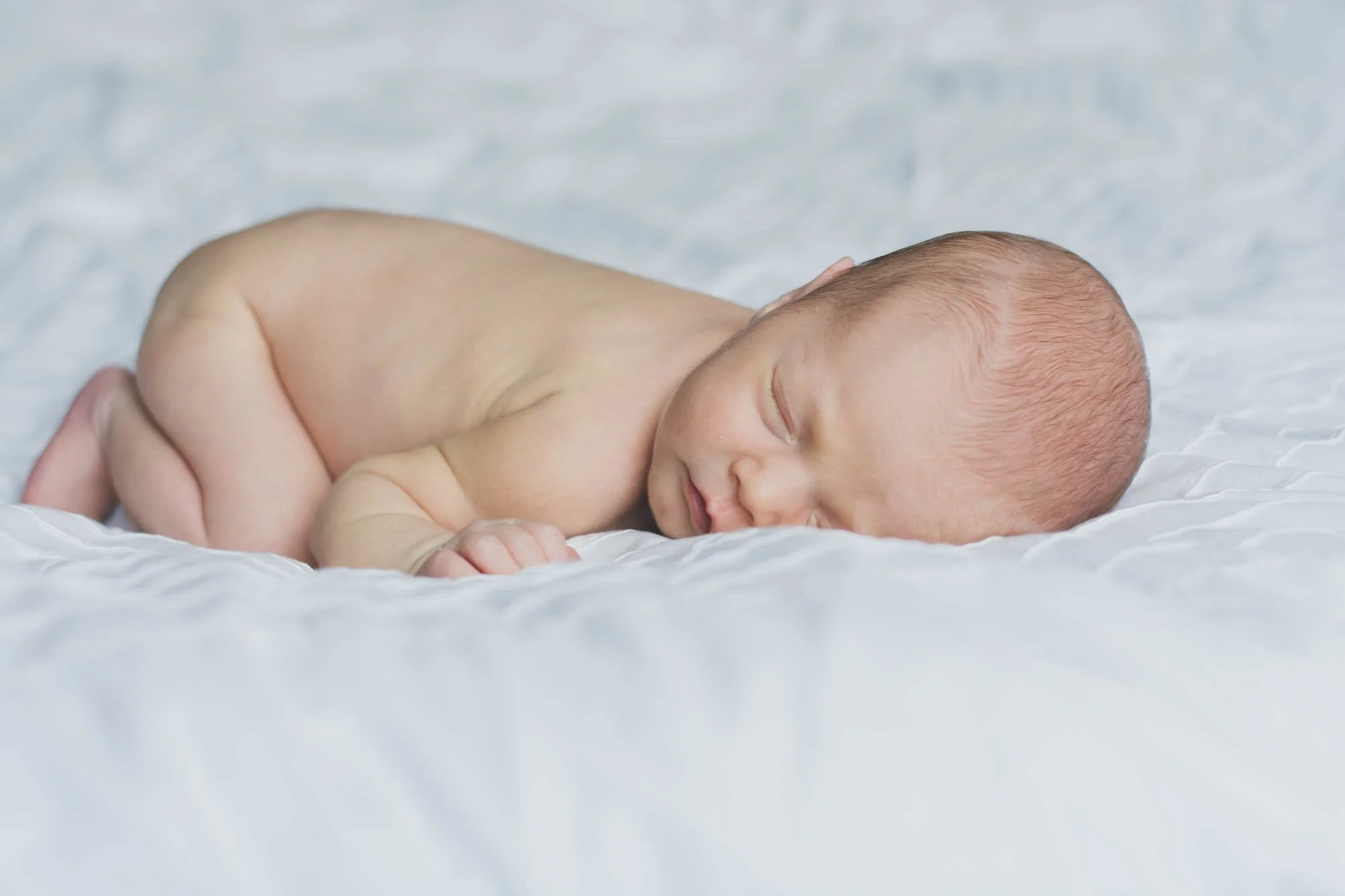 Een slapende baby ligt op een witte, zachte deken.