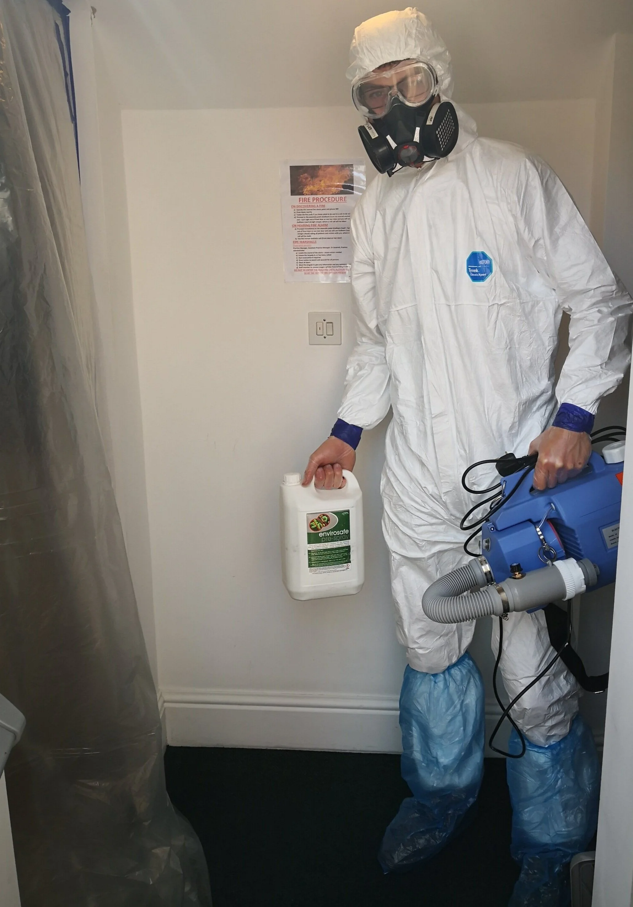 Person in protective hazmat suit holding a container of disinfectant spray