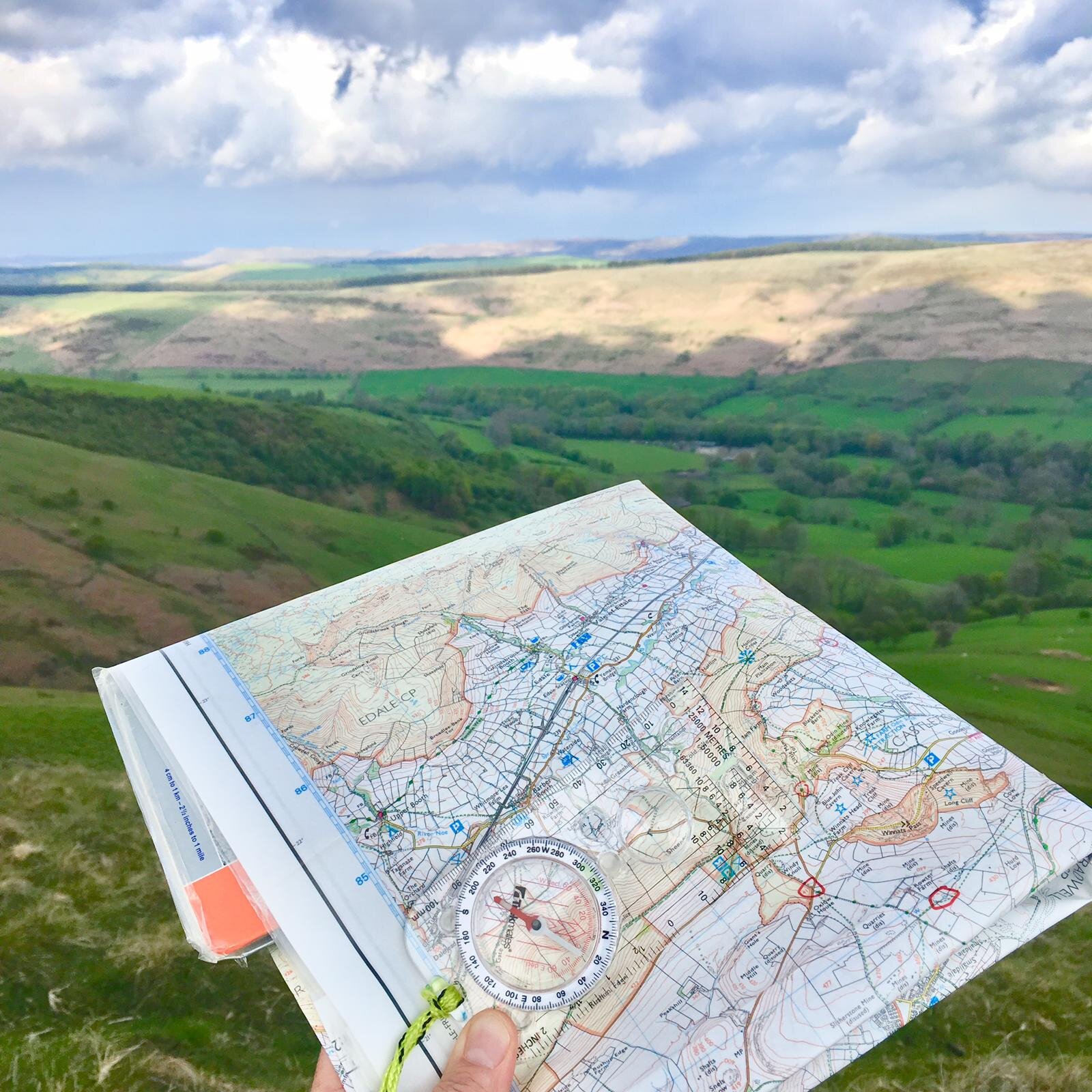 Person holding a map and compass over a hilly landscape