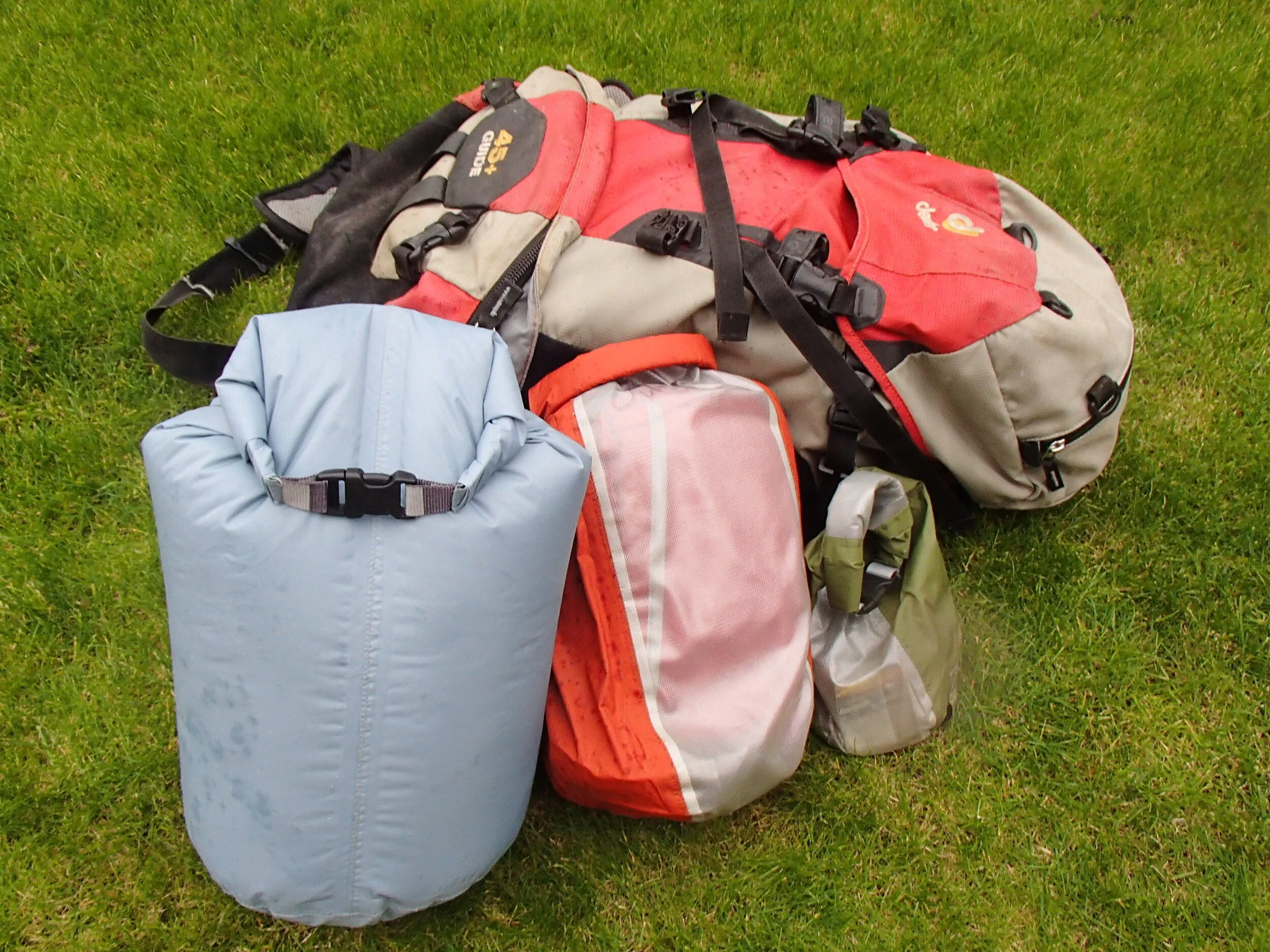 A selection of walkers rucksack and dry bags laid out on the grass.