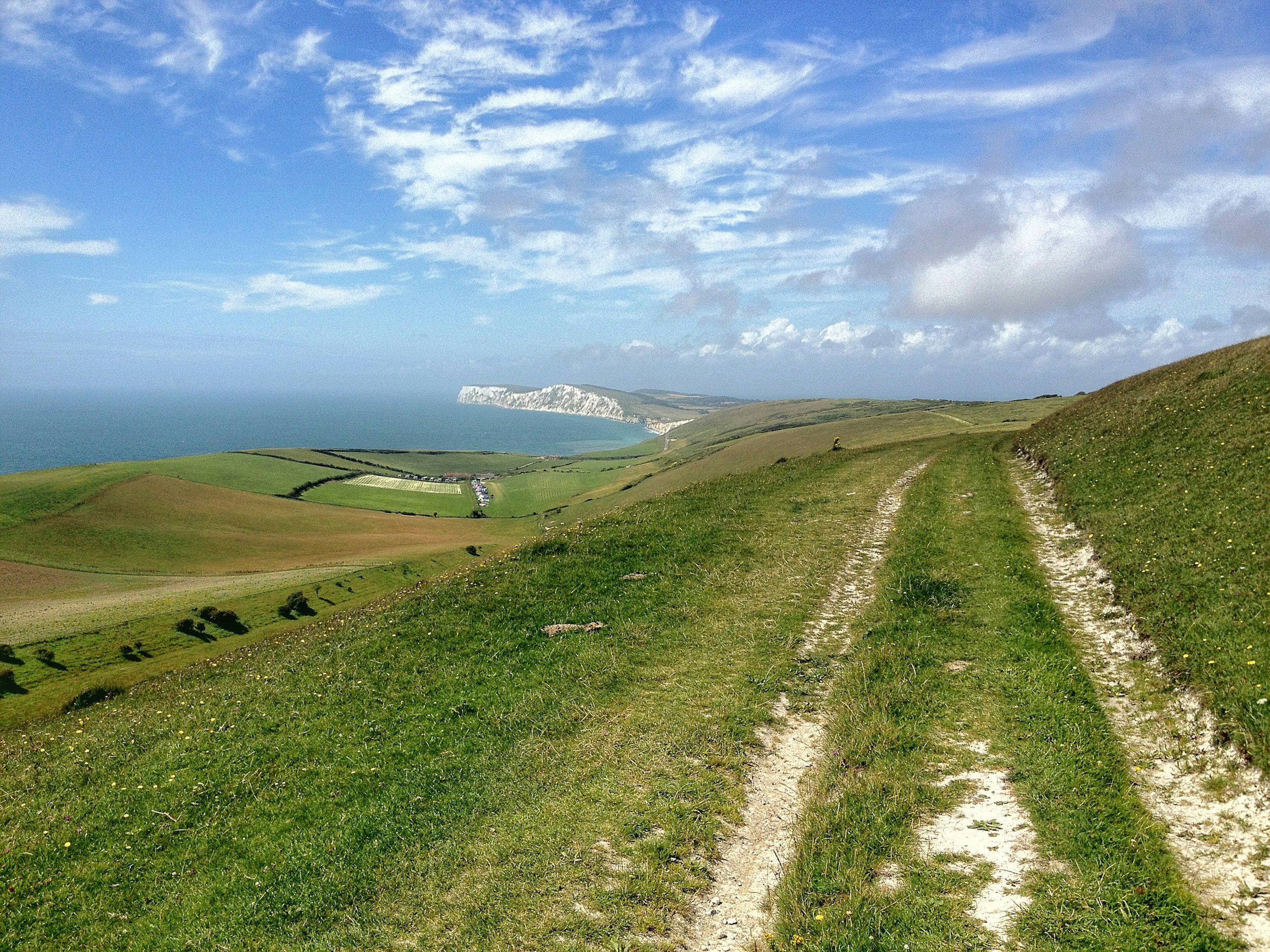 Grassy path on a hill overlooking a coastal landscape with cliffs and ocean under a blue sky with clouds.